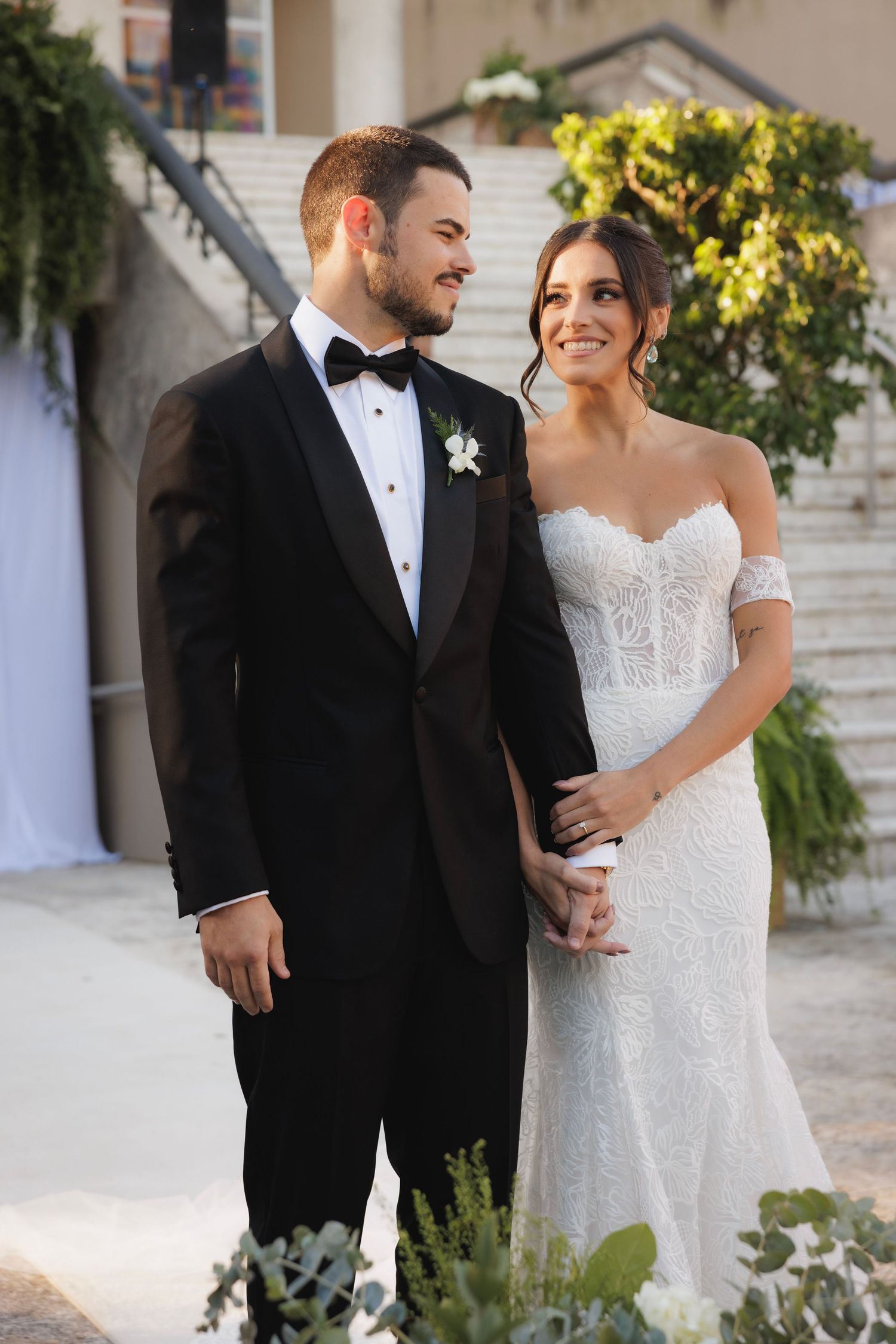 A romantic wedding portrait of a couple in formal attire standing together against a garden backdrop.