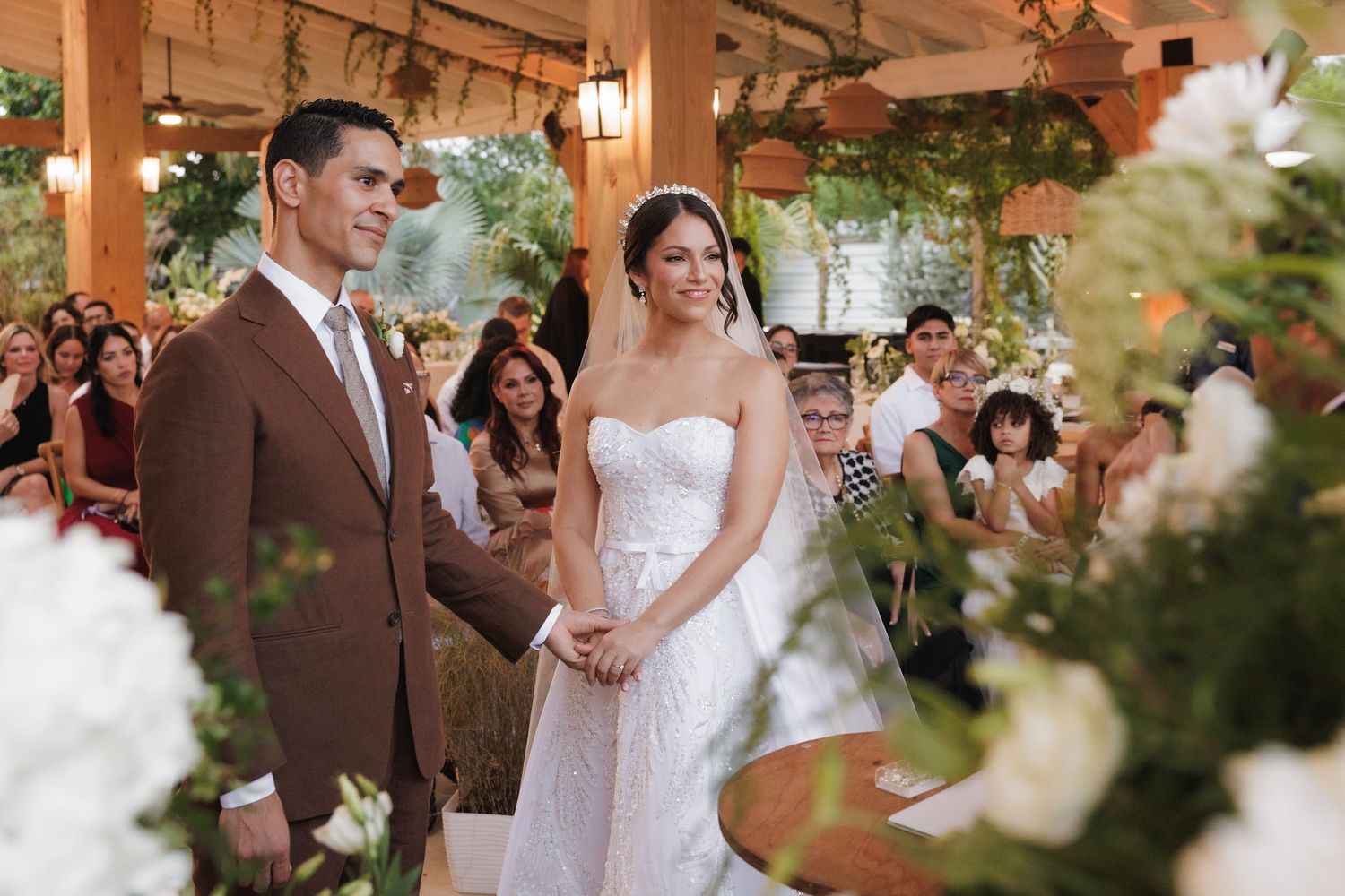 Wedding couple shares romantic moments in an elegant venue decorated with white flowers and wooden beams.