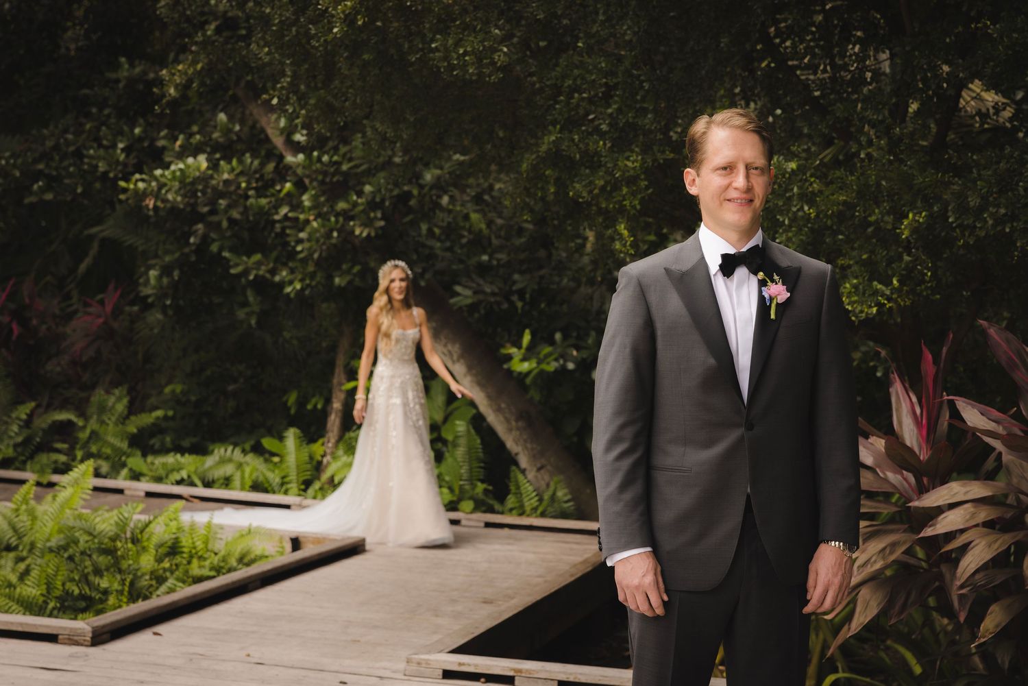 A wedding first look moment captured in a lush garden setting with a bride and groom on a wooden deck.