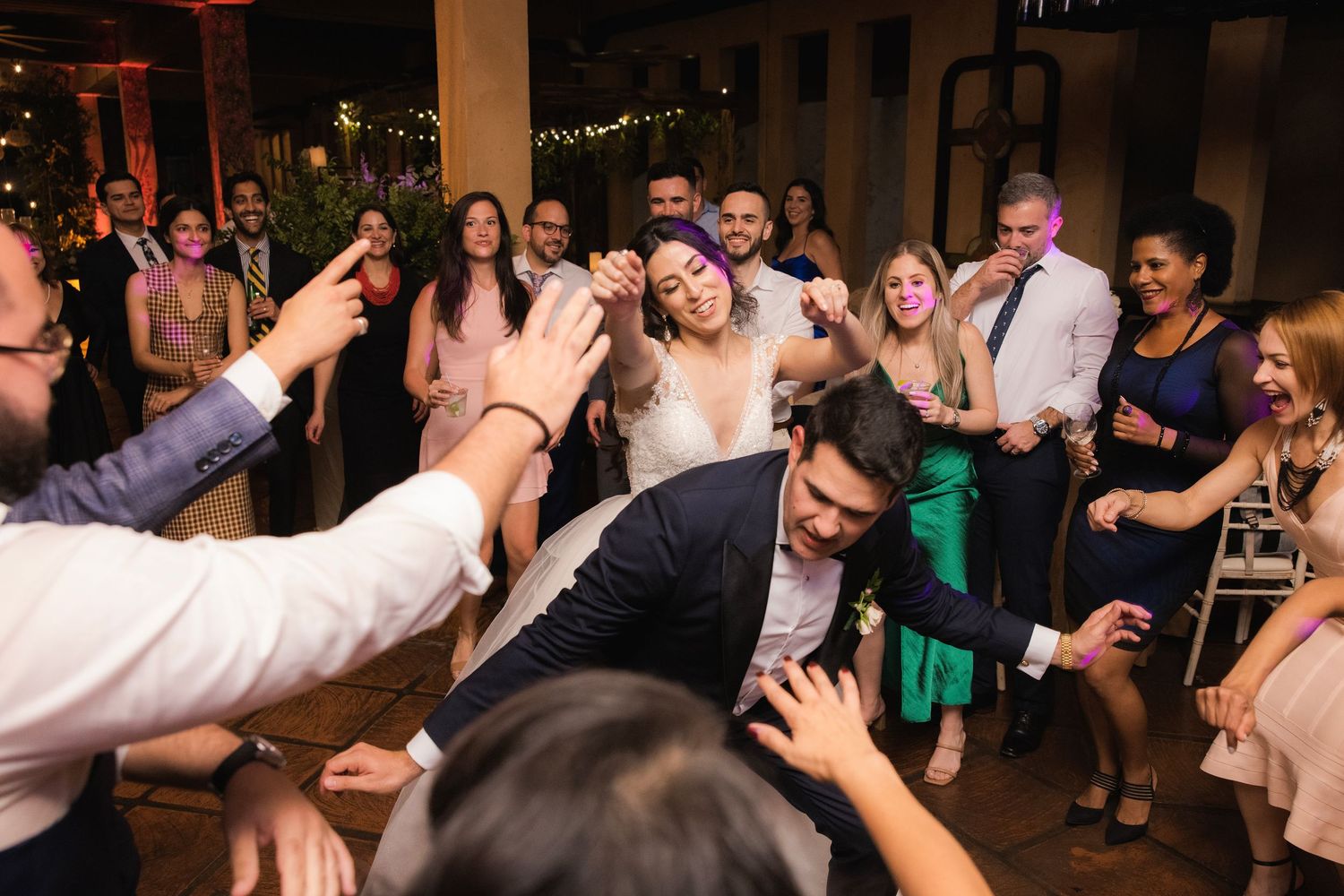 Wedding guests dancing and celebrating enthusiastically on a crowded dance floor at an evening reception.