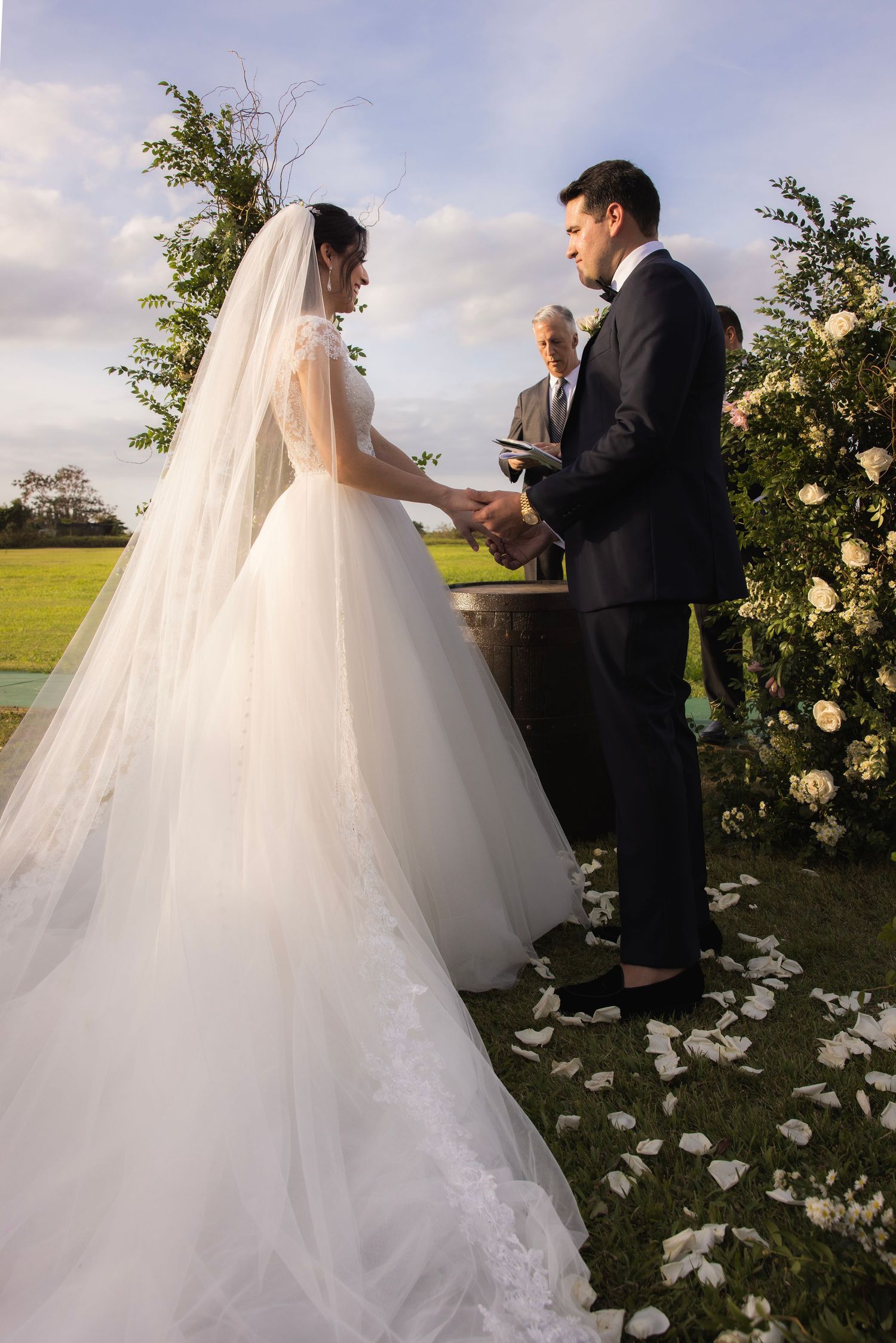 A romantic sunset wedding ceremony moment shows a couple exchanging vows in a beautiful garden setting with rose petals.