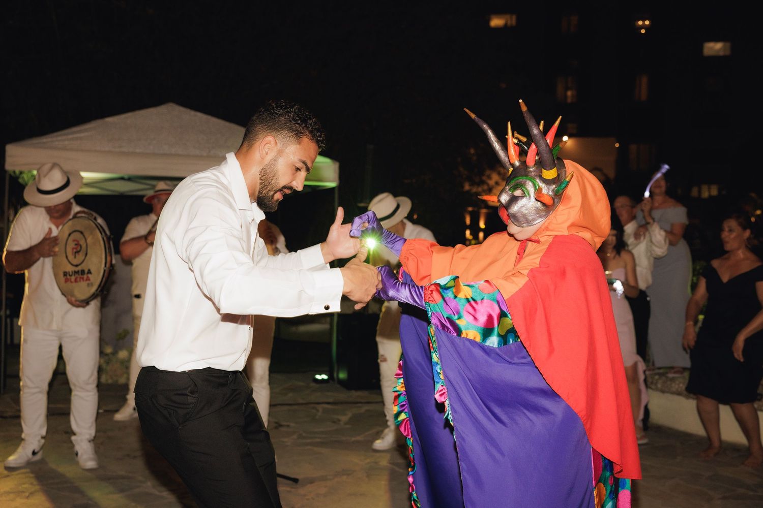 Dancers in colorful outfits enjoying themselves on a dimly lit dance floor at an evening celebration.