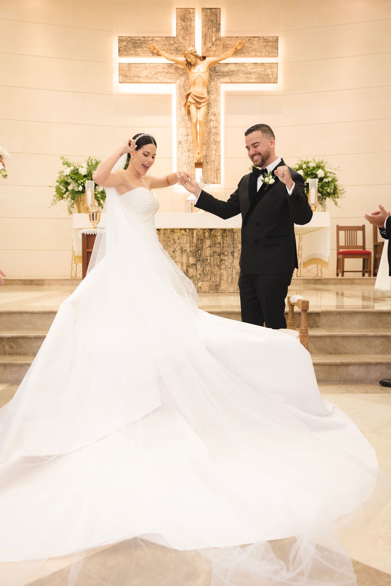 Bride and groom dance together in a church with white decor and crucifixes on display during their wedding celebration.