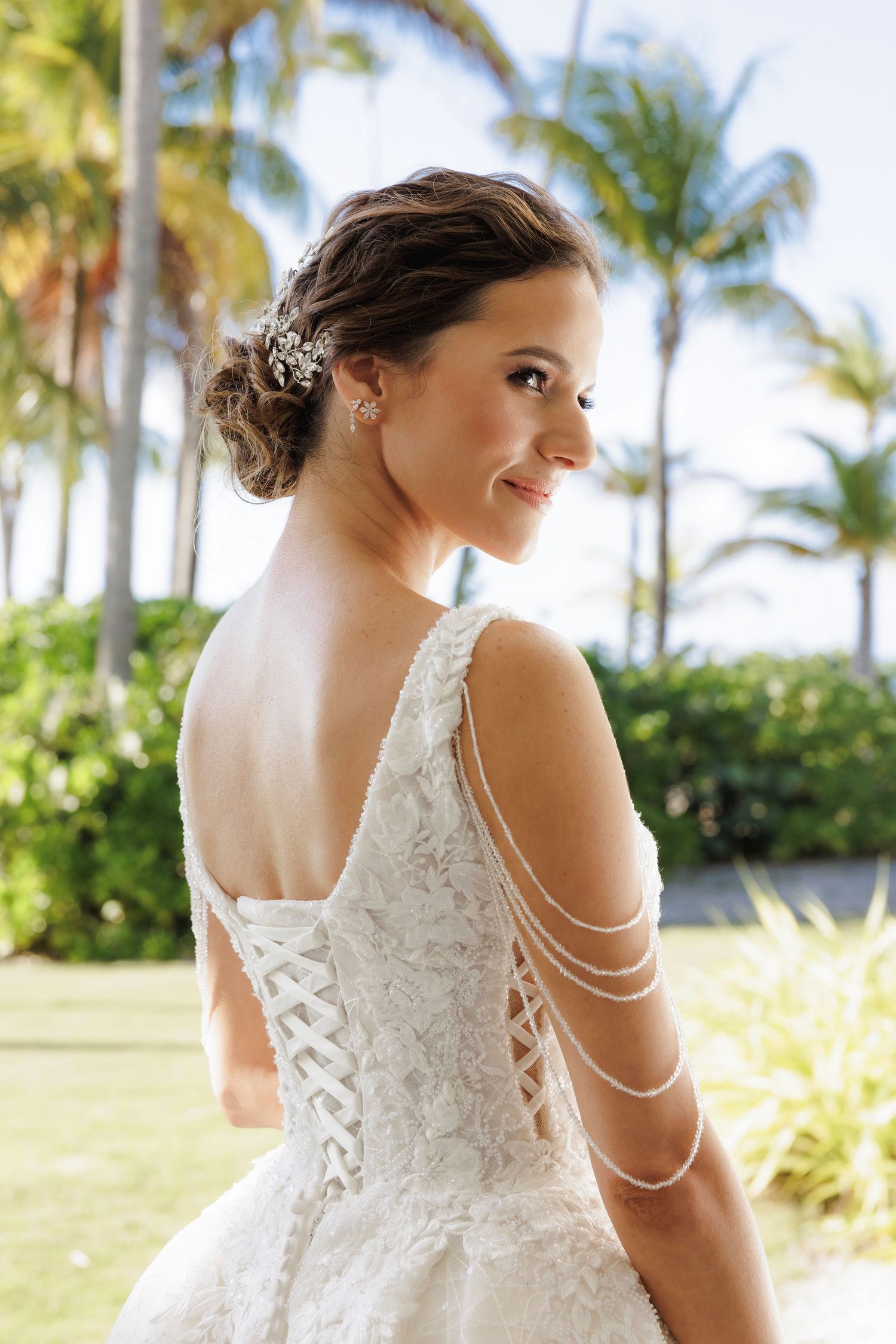 A wedding dress with delicate pearl shoulder straps and lace detailing in a tropical setting with palm trees.