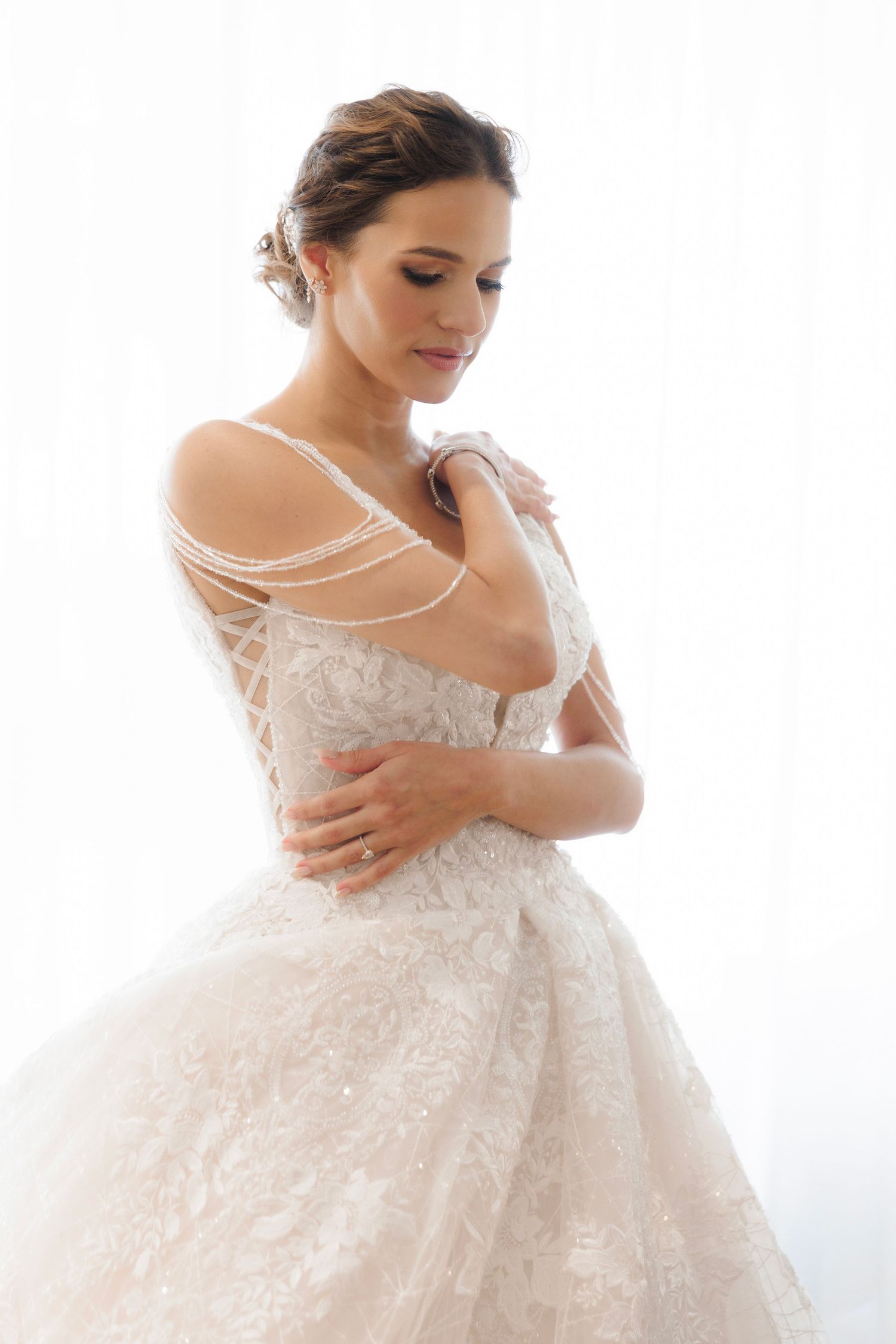 White lace wedding dress with off-shoulder straps and delicate pearl details shown in elegant bridal portrait.