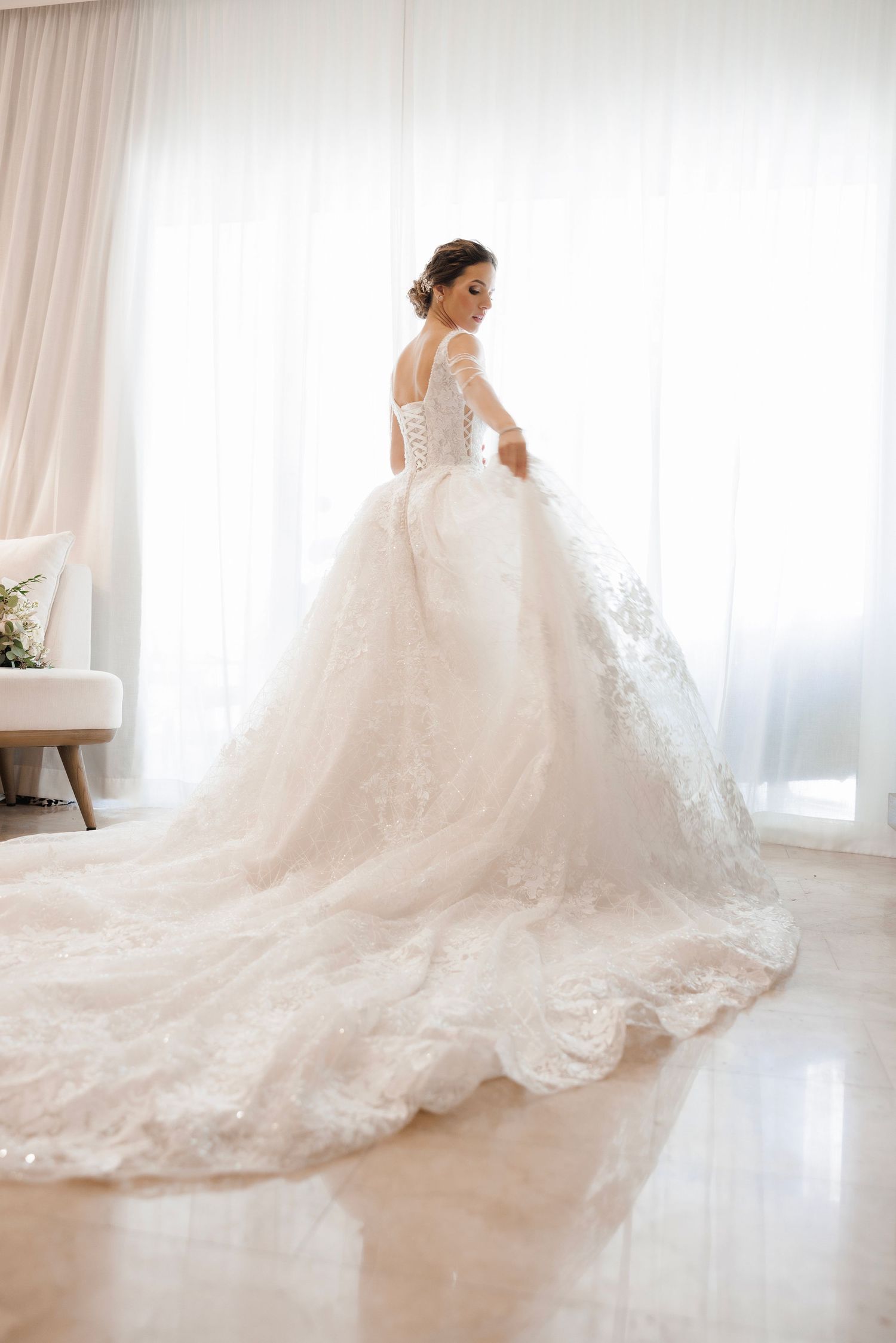 Elegant white wedding gown with long lace trim train and corset back details photographed in bright natural light.