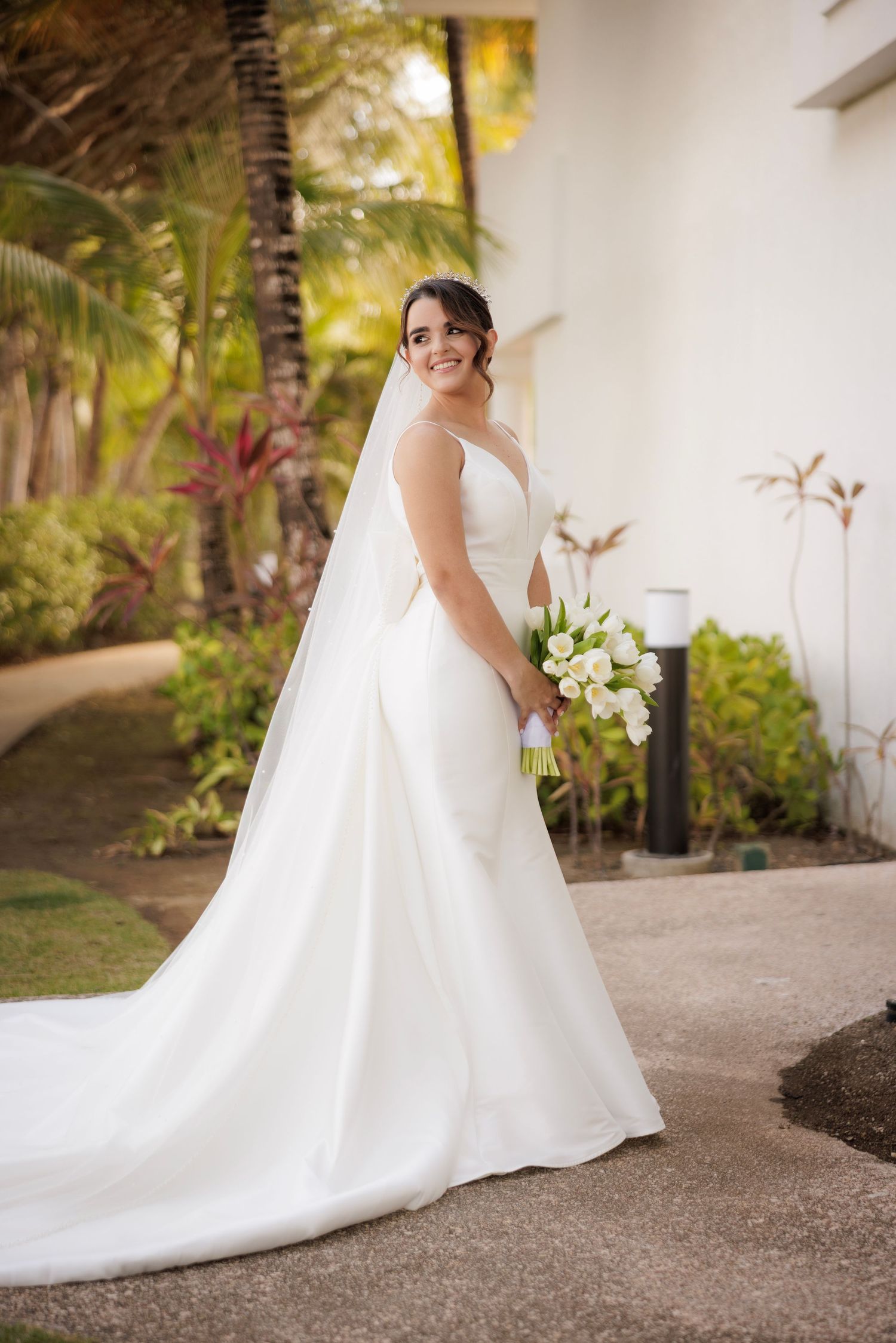 A bride in a classic white ballgown wedding dress poses gracefully in a garden setting with her long train flowing behind her.