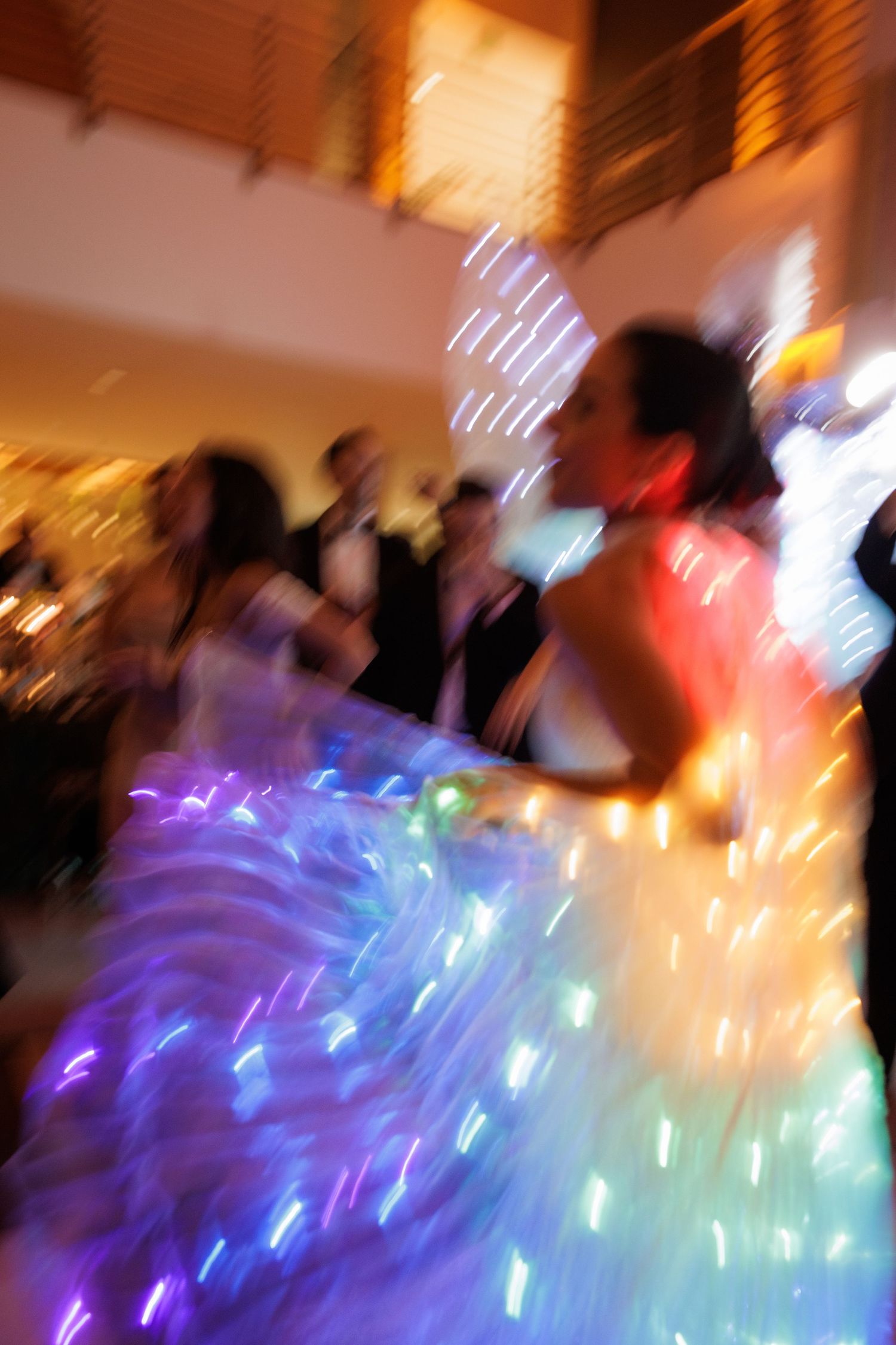 Abstract motion blur of dancers with illuminated LED wings creating colorful light trails at a celebration.