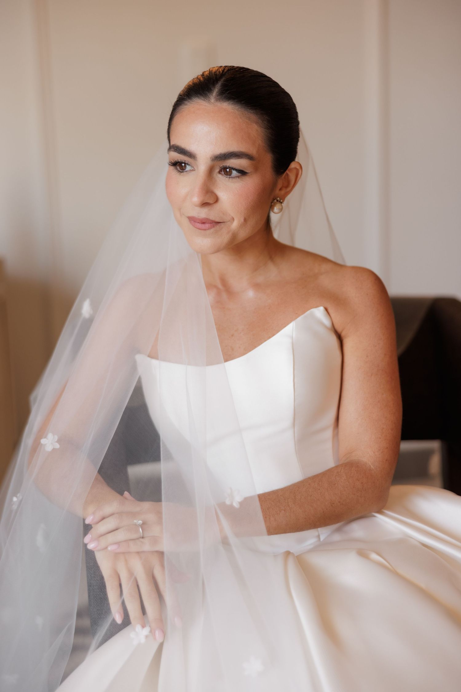 A bride in a classic white wedding dress adjusts her flowing veil during wedding preparations.