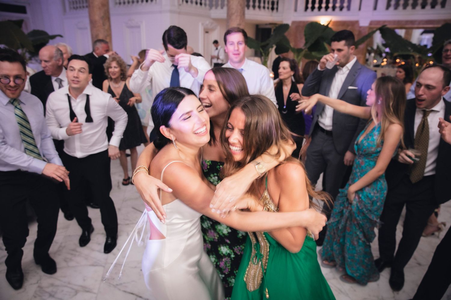 Guests celebrating on a packed dance floor at an elegant wedding reception with classic architecture.