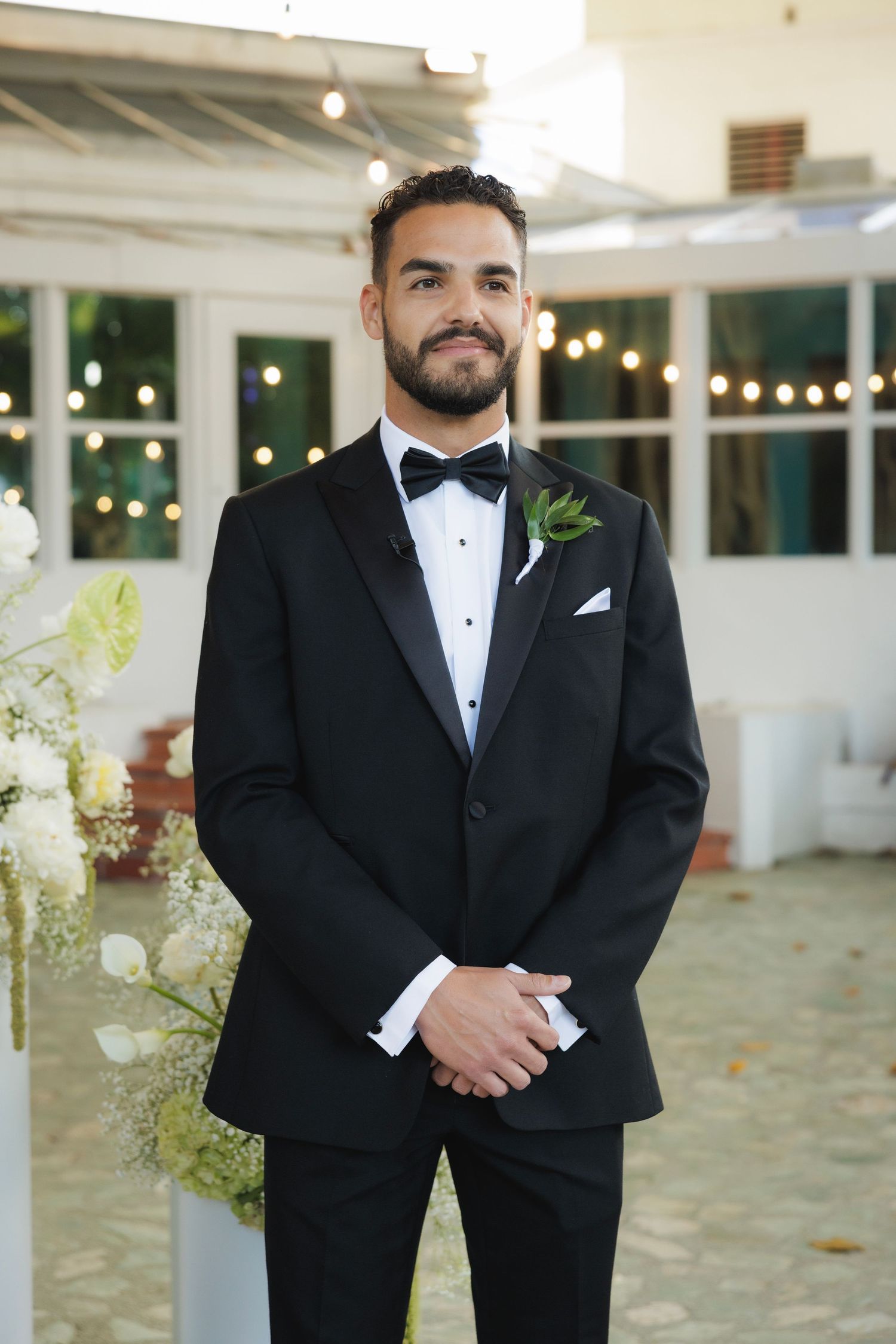 Formal portrait series showing groom in classic black tuxedo and white pocket square in sunlit wedding venue.