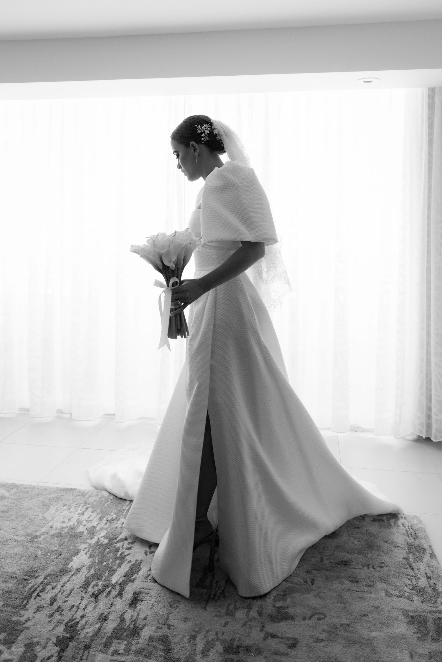 A black and white portrait of a bride in an elegant split dress holding a bouquet.