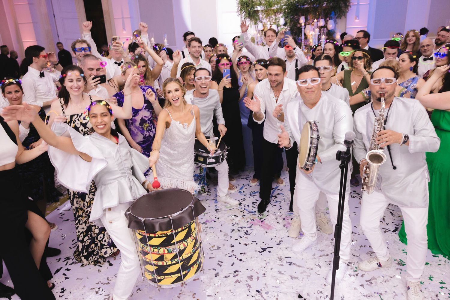 Wedding party celebrating with musicians and confetti on the dance floor during reception with purple lighting effects.