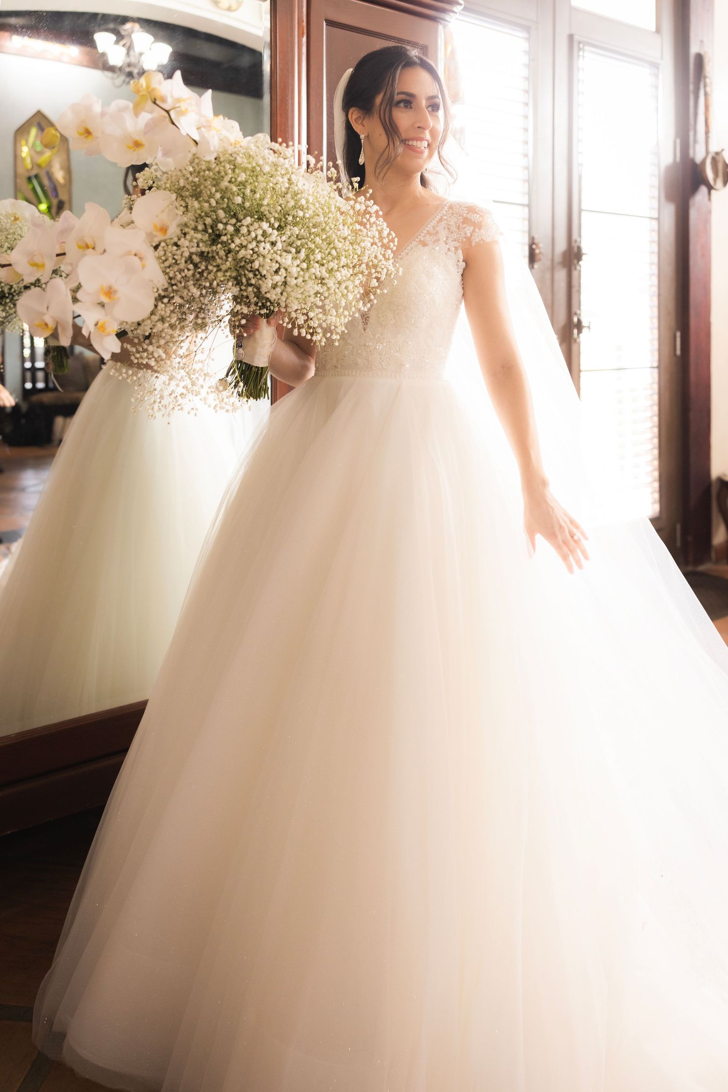 Beautiful bride in voluminous white ballgown poses with delicate white orchids and baby's breath bouquet.