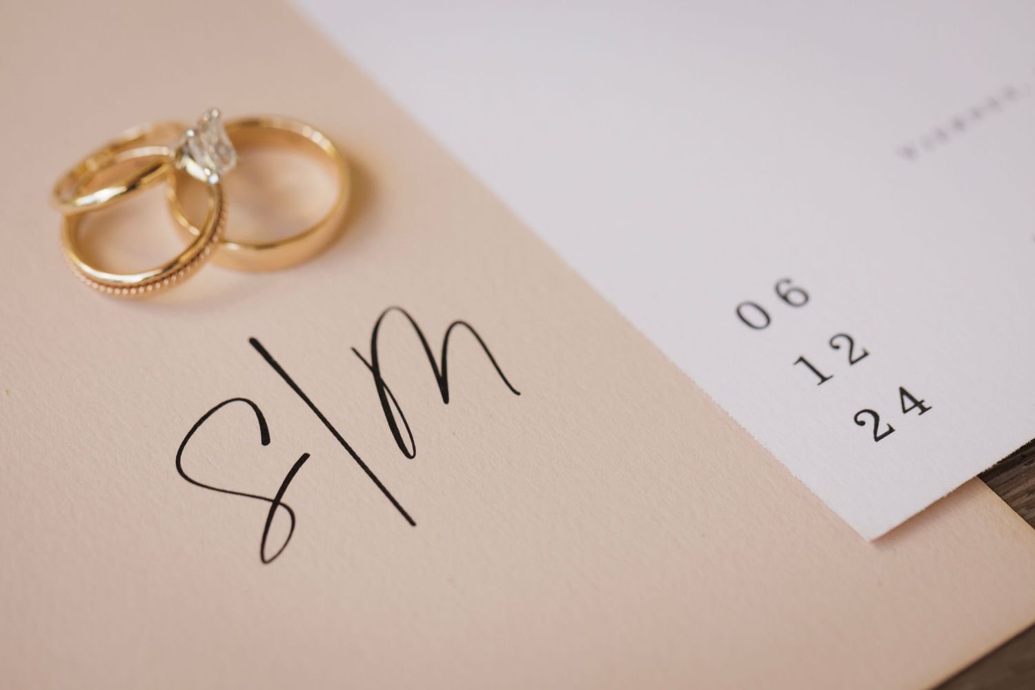 Golden wedding rings and elegant stationery details arranged on a light beige surface in minimalist style.