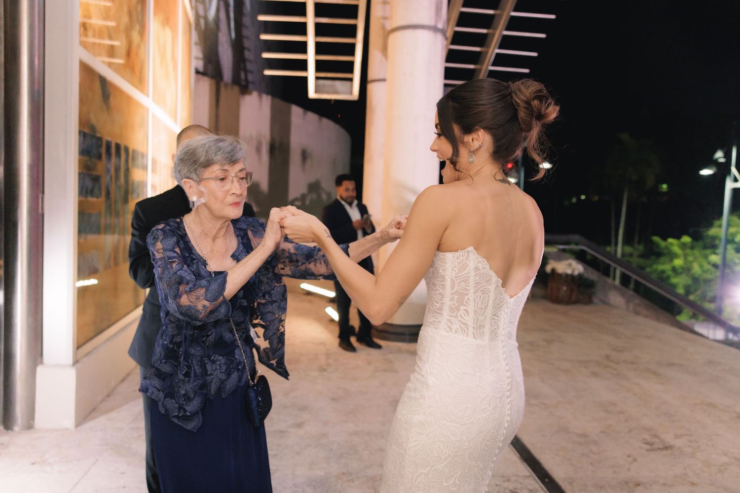 At a wedding reception, dancers move to the music while guests mingle in an elegantly lit indoor venue.