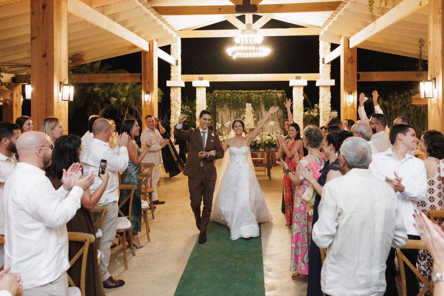 Wedding guests dancing and celebrating in a rustic indoor venue with wooden ceiling beams.