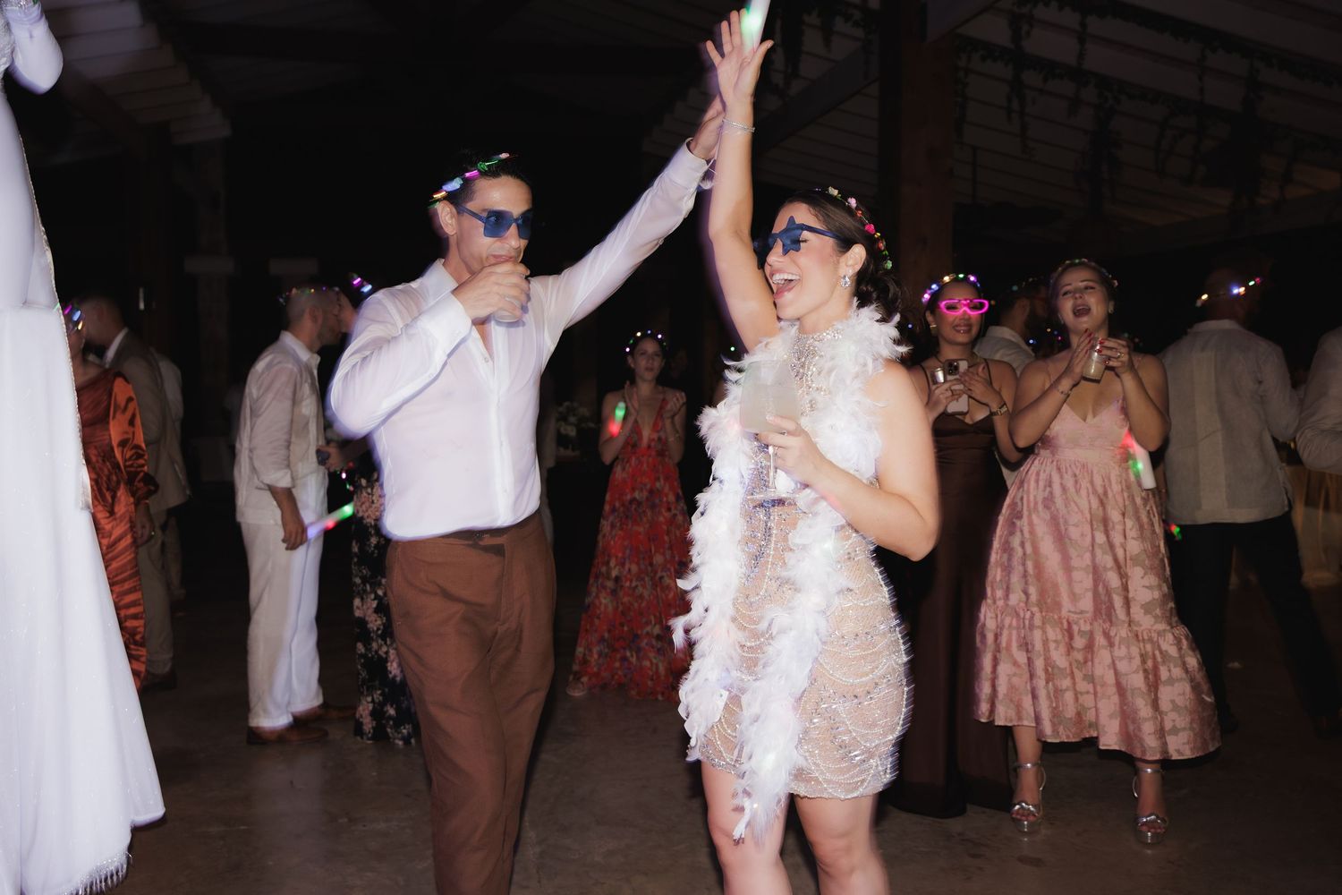 People dancing and celebrating with raised arms on a dimly lit dance floor.