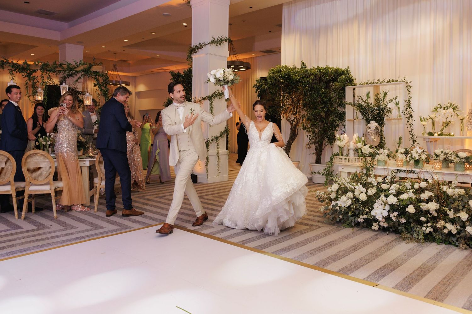 Wedding dress gown train being arranged and styled on a gray and white striped floor at luxurious venue entrance.