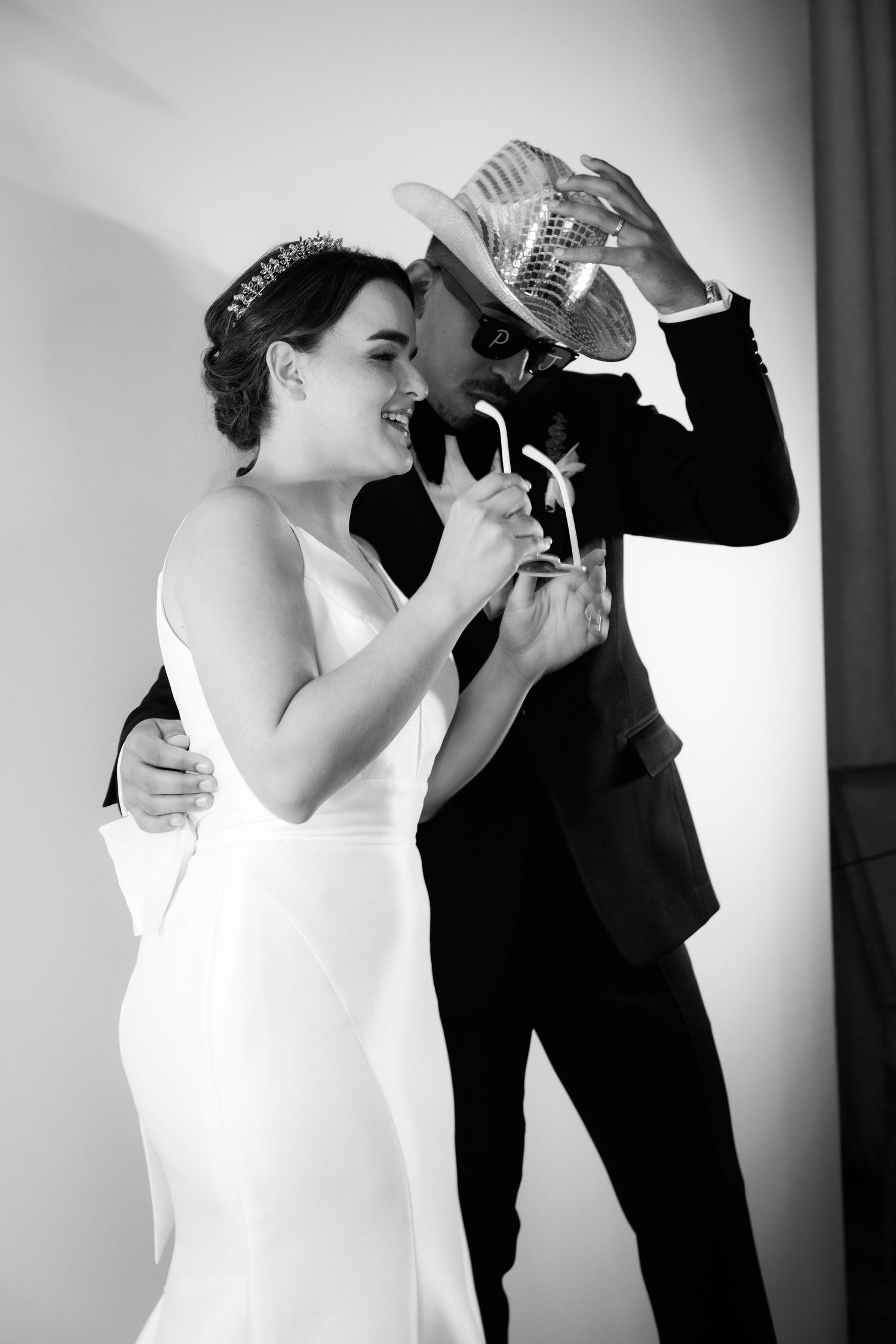 Black and white wedding photo of couple playfully interacting, bride in sleek white dress and groom in dark suit.