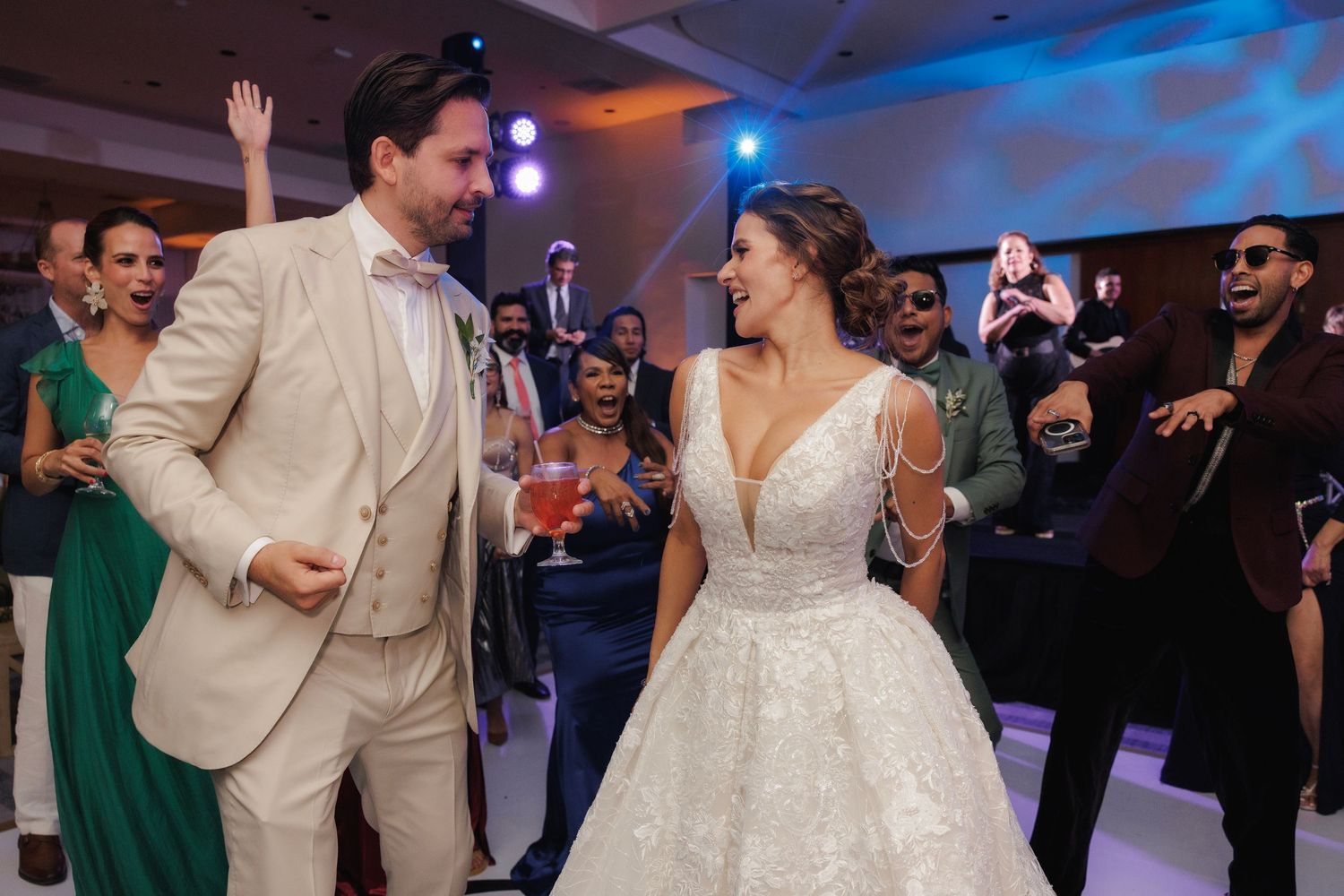 Newlyweds and wedding guests dance joyfully on an illuminated dance floor at an elegant indoor reception.