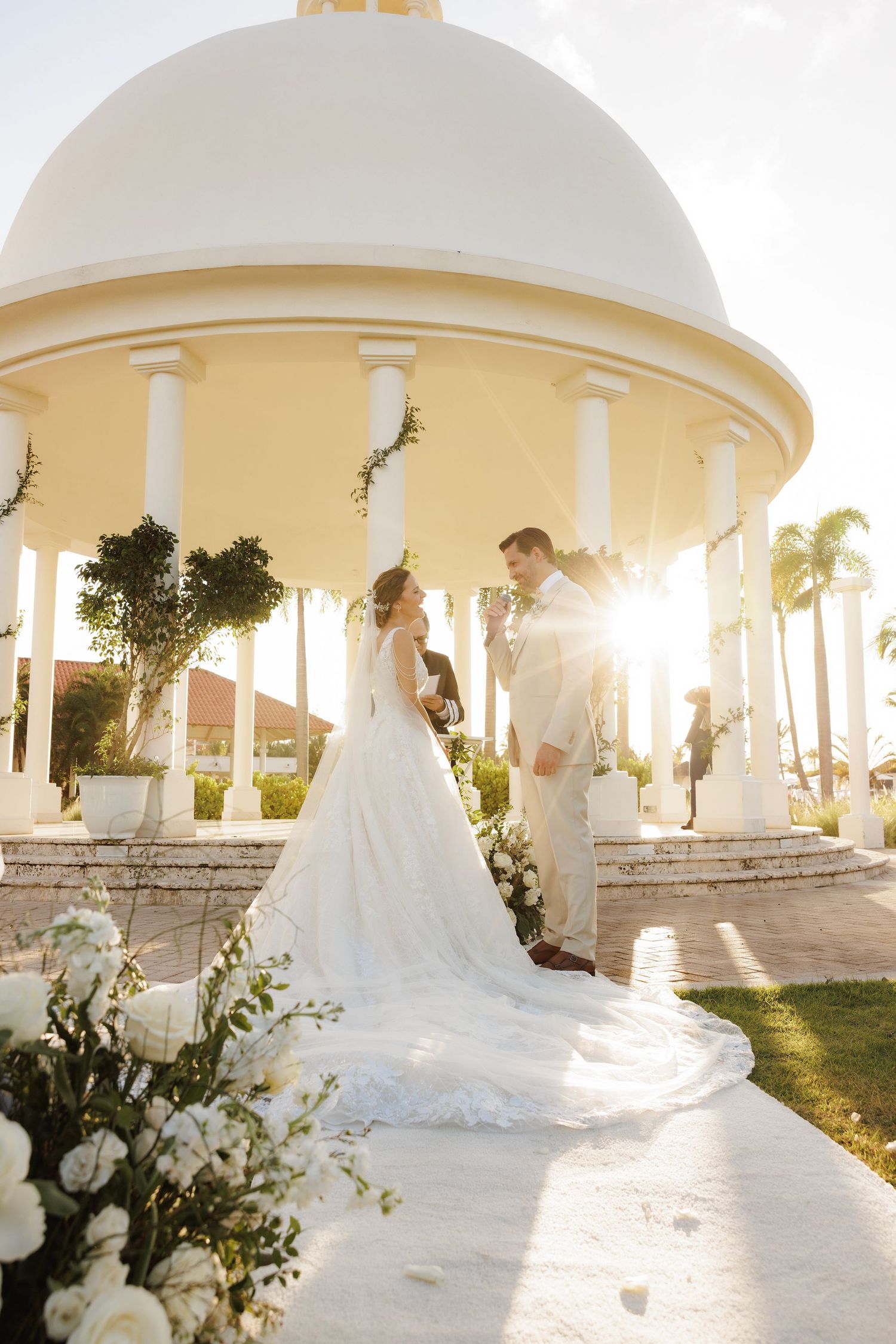 A series of elegant wedding photographs showing bride and groom under white archways at sunset with floral decorations.
