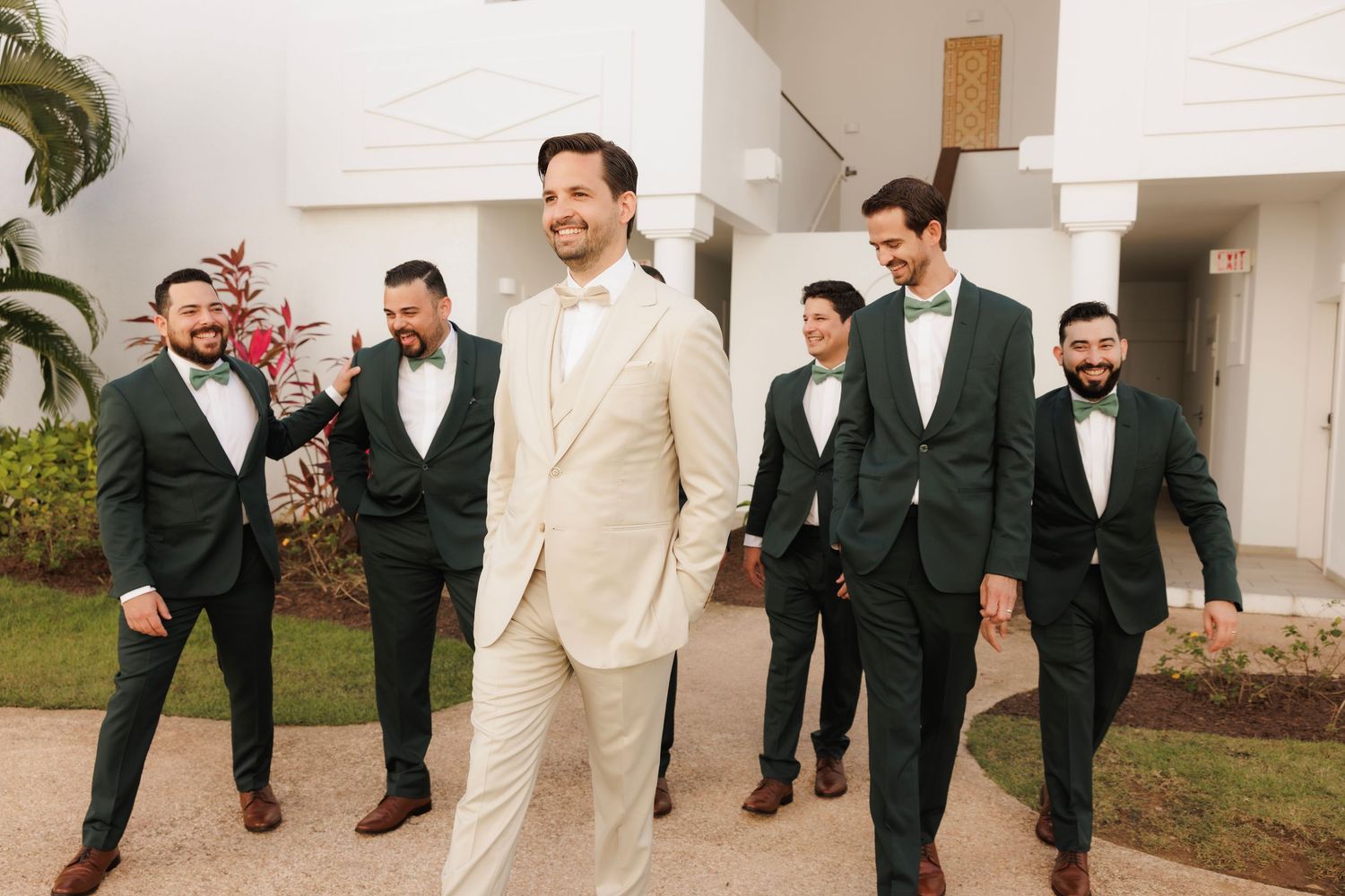 A group in formal attire walks along a path while smiling and laughing together during an outdoor event.