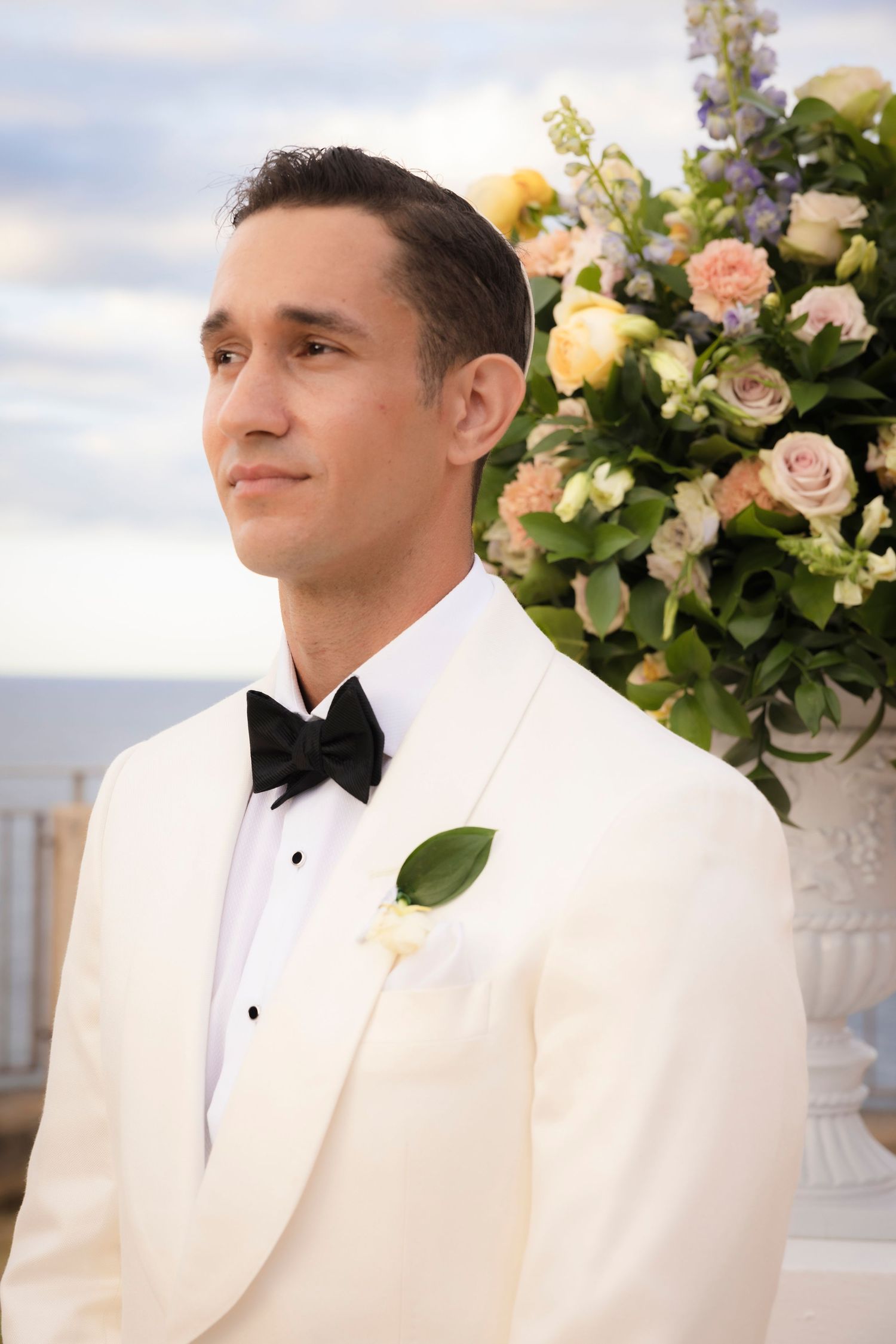 Close-up details of white tuxedo and floral arrangements at outdoor wedding ceremony.