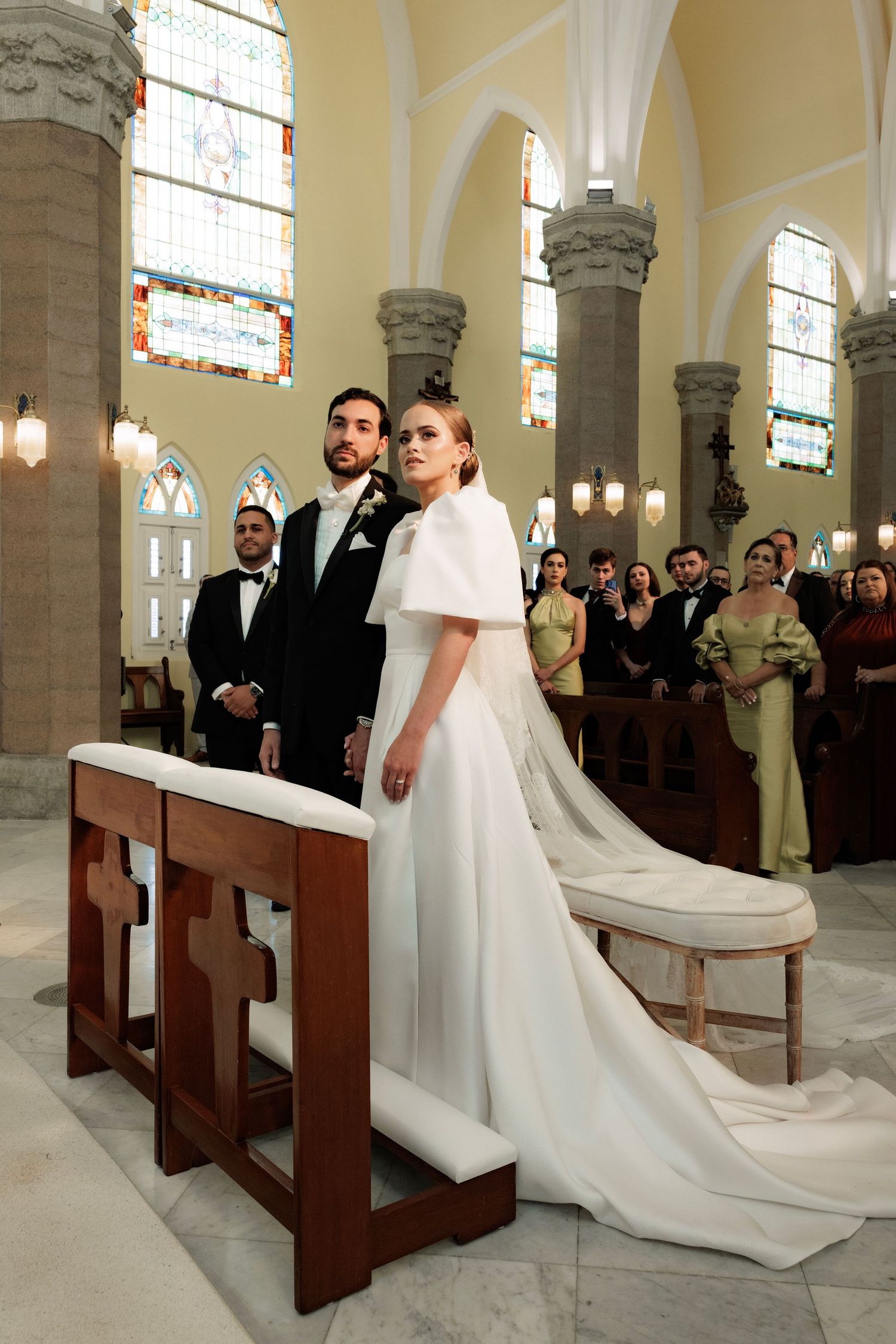 A wedding ceremony takes place in an elegant church with stone columns and stained glass windows.