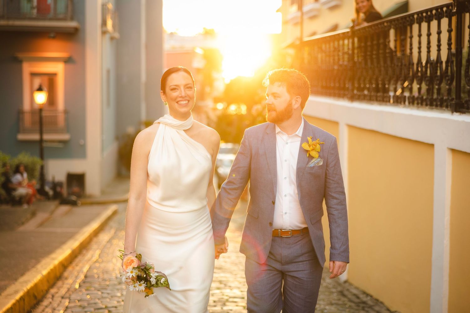 A romantic golden hour portrait of a couple walking together down a sun-lit cobblestone street.