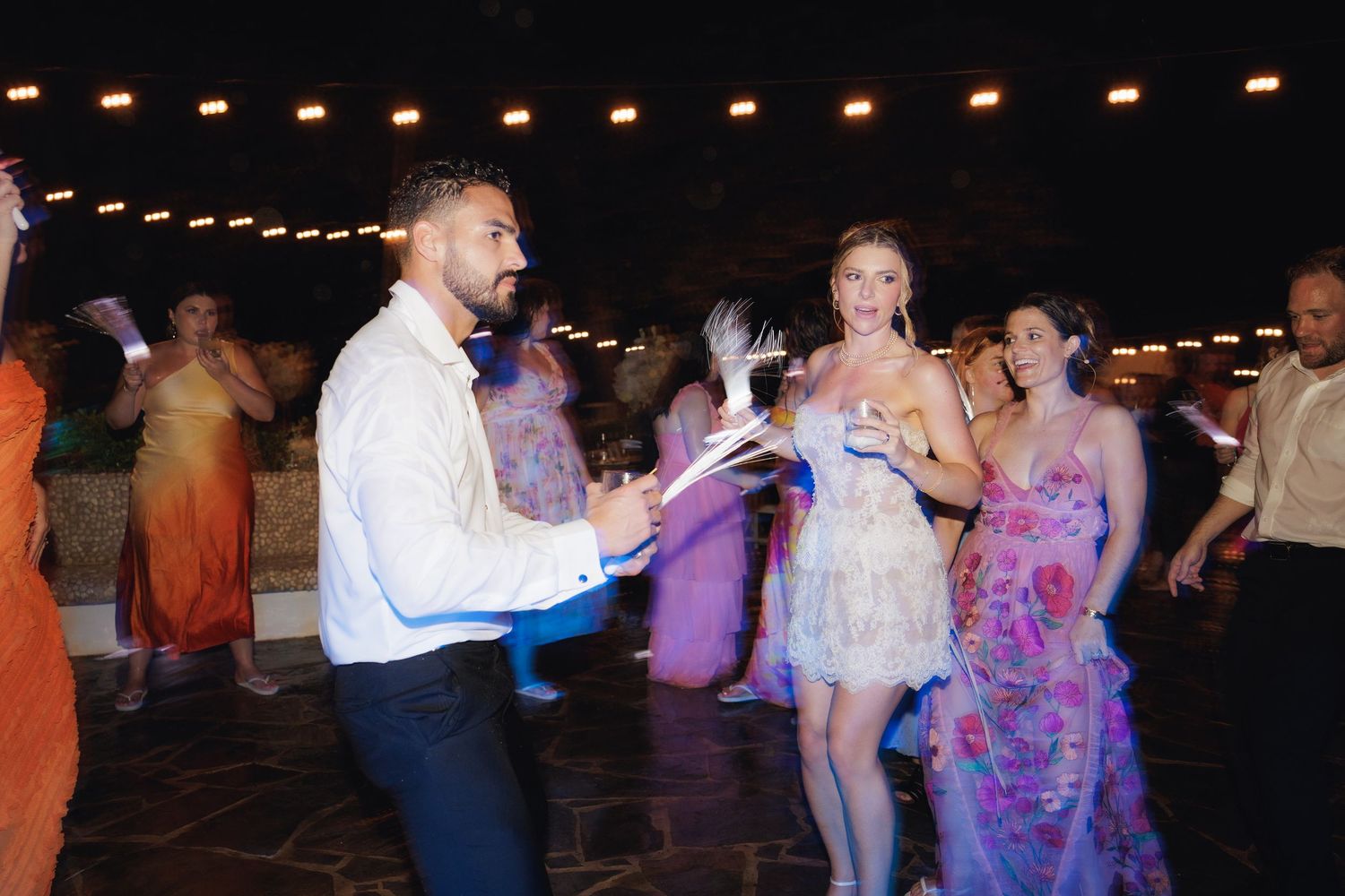 Guests celebrate and dance together at an evening reception, illuminated by warm overhead lighting.