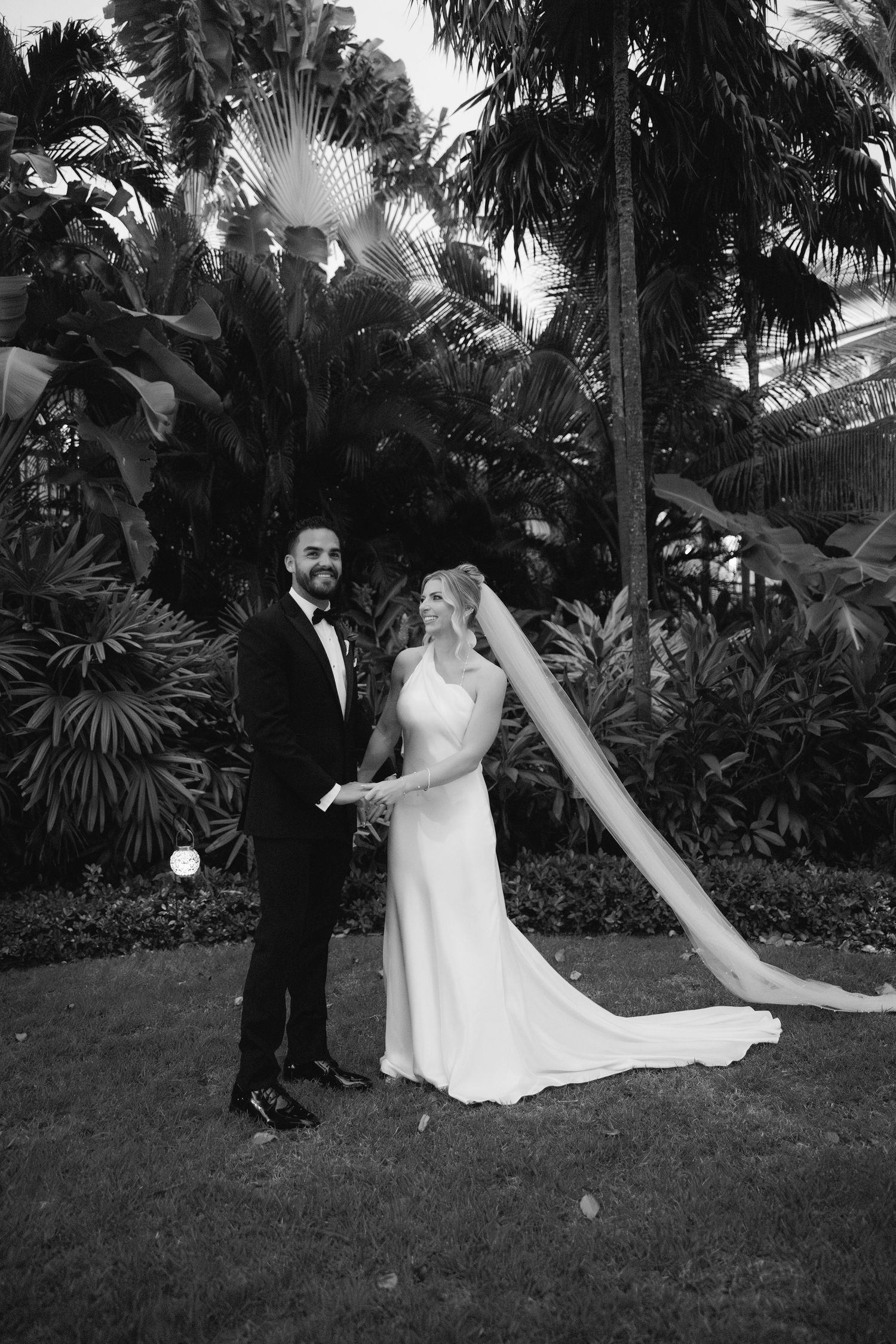 Wedding couple playfully posing in tropical garden setting.
