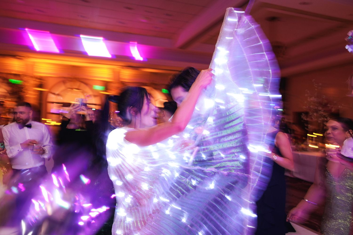 Purple and pink party lights create an atmospheric glow across a crowded dance floor.