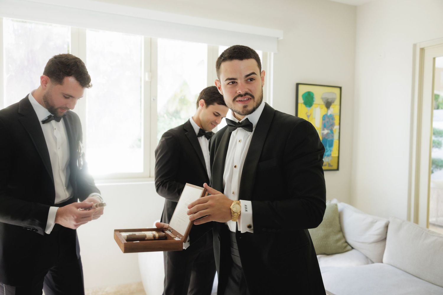 Wedding party members in tuxedos preparing in a bright modern room.
