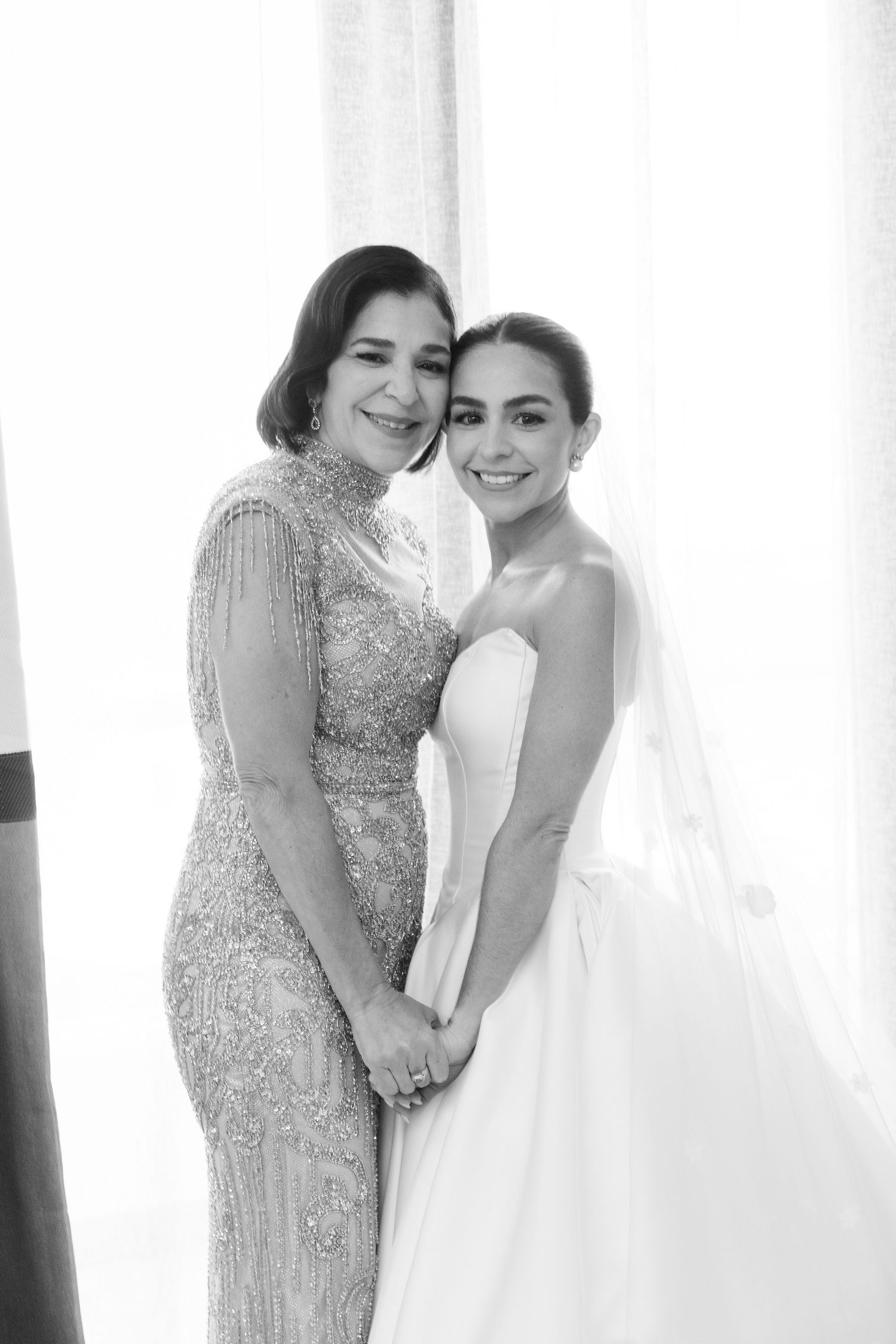 A tender moment shared between a bride in white and another person wearing a sparkly beaded dress at a wedding.