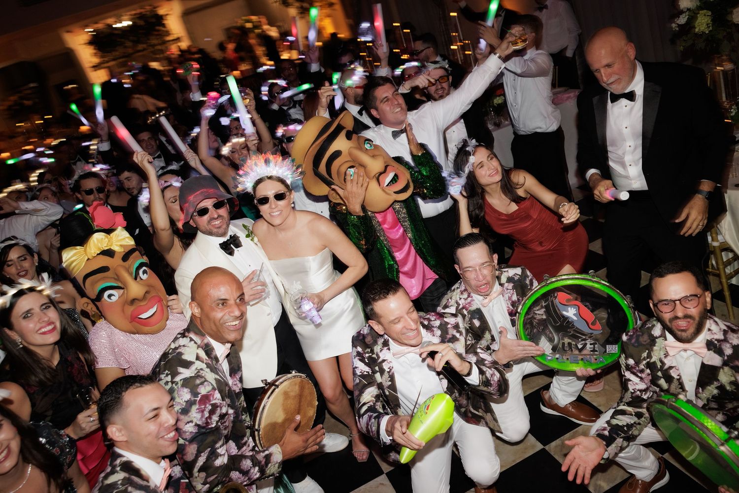 A large crowd of party-goers celebrating with glow sticks and neon accessories at a nighttime event.