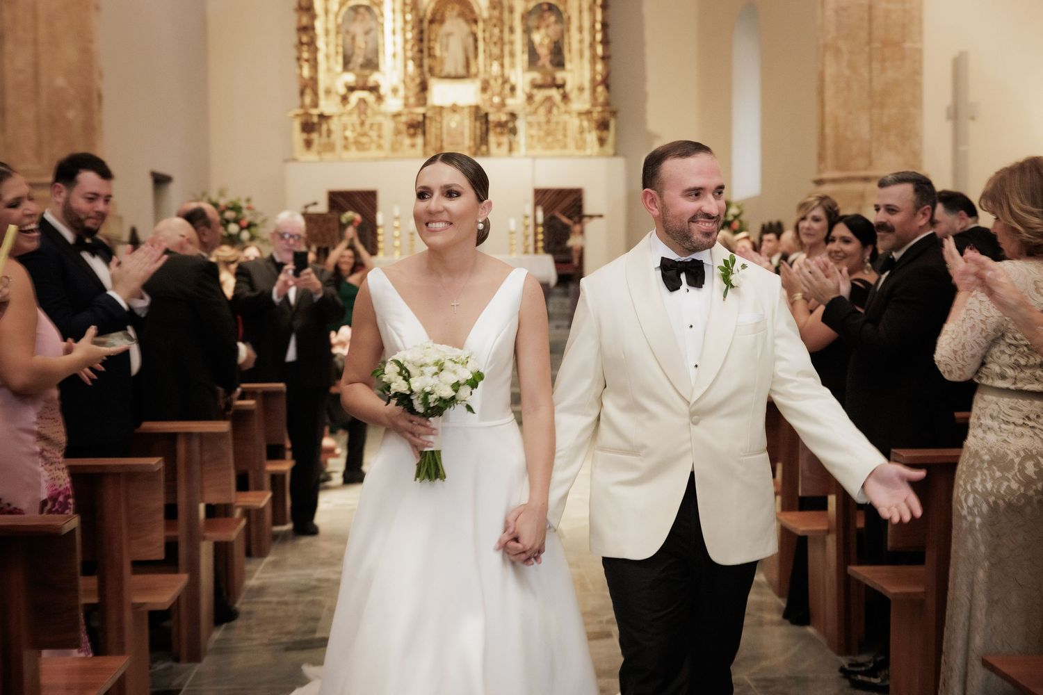 Wedding ceremony celebration in a church with ornate golden altar and wooden pews.
