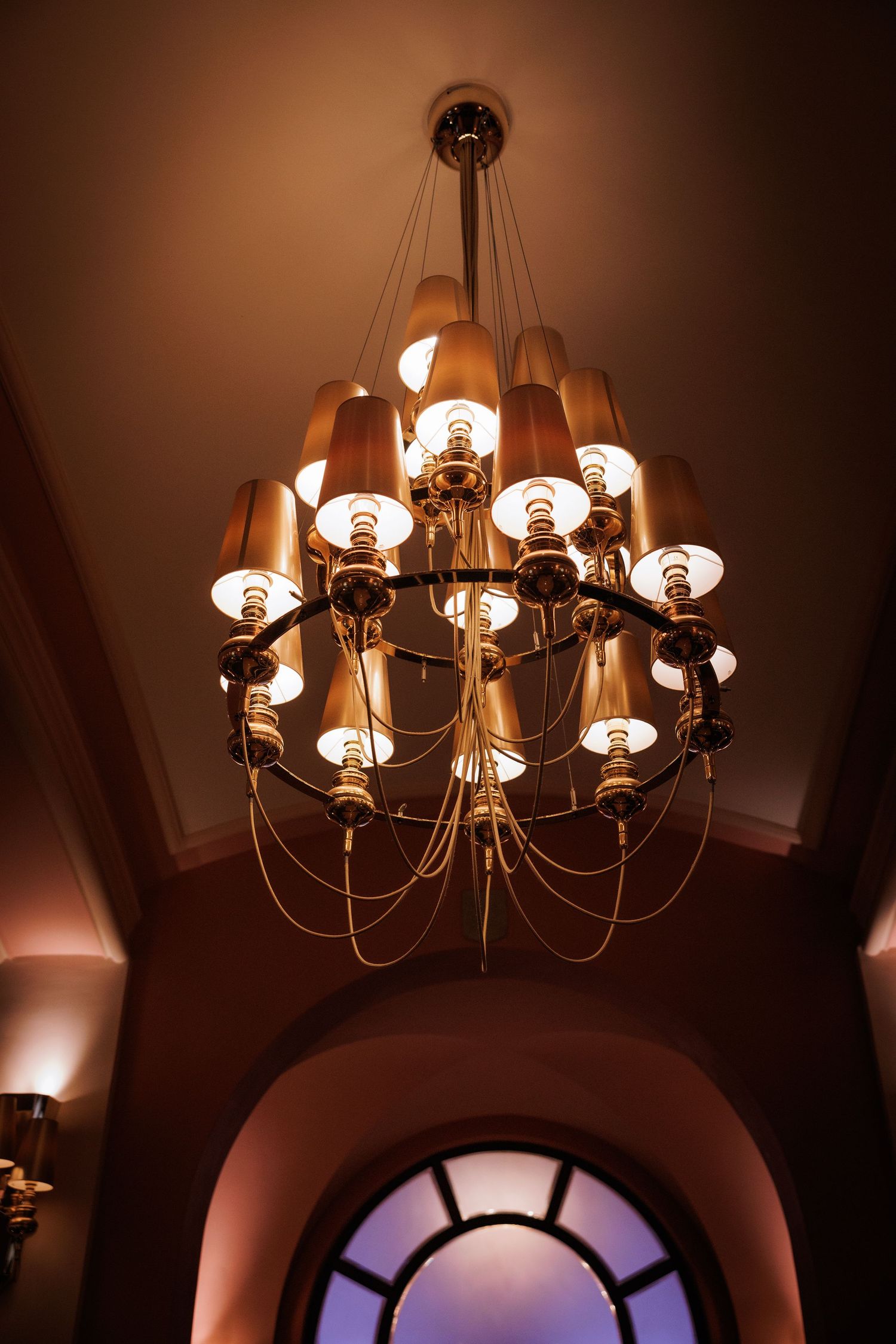 Elegant chandelier with multiple glass shades casting a warm ambient glow in an arched entryway.