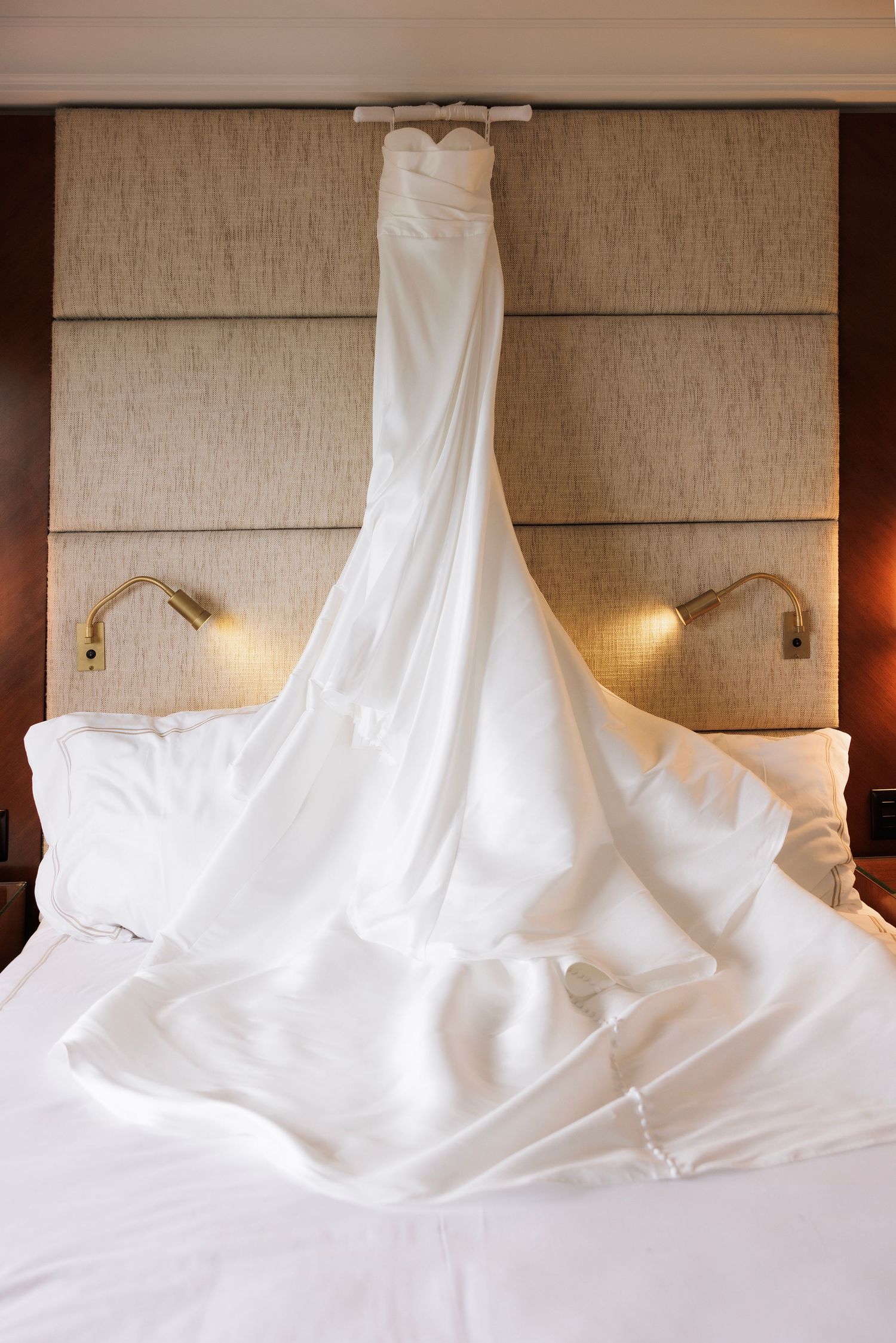 White wedding dress elegantly displayed on a hotel bed with soft lighting and neutral decor.