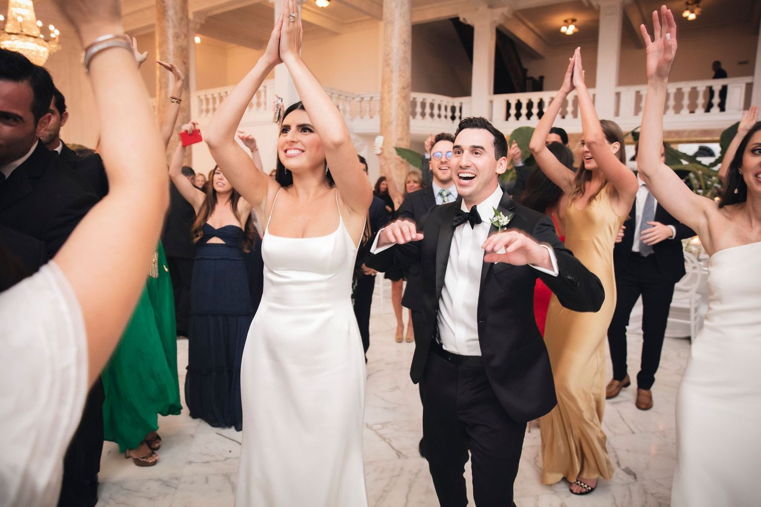 Wedding guests dancing together on a ballroom floor during a reception celebration.