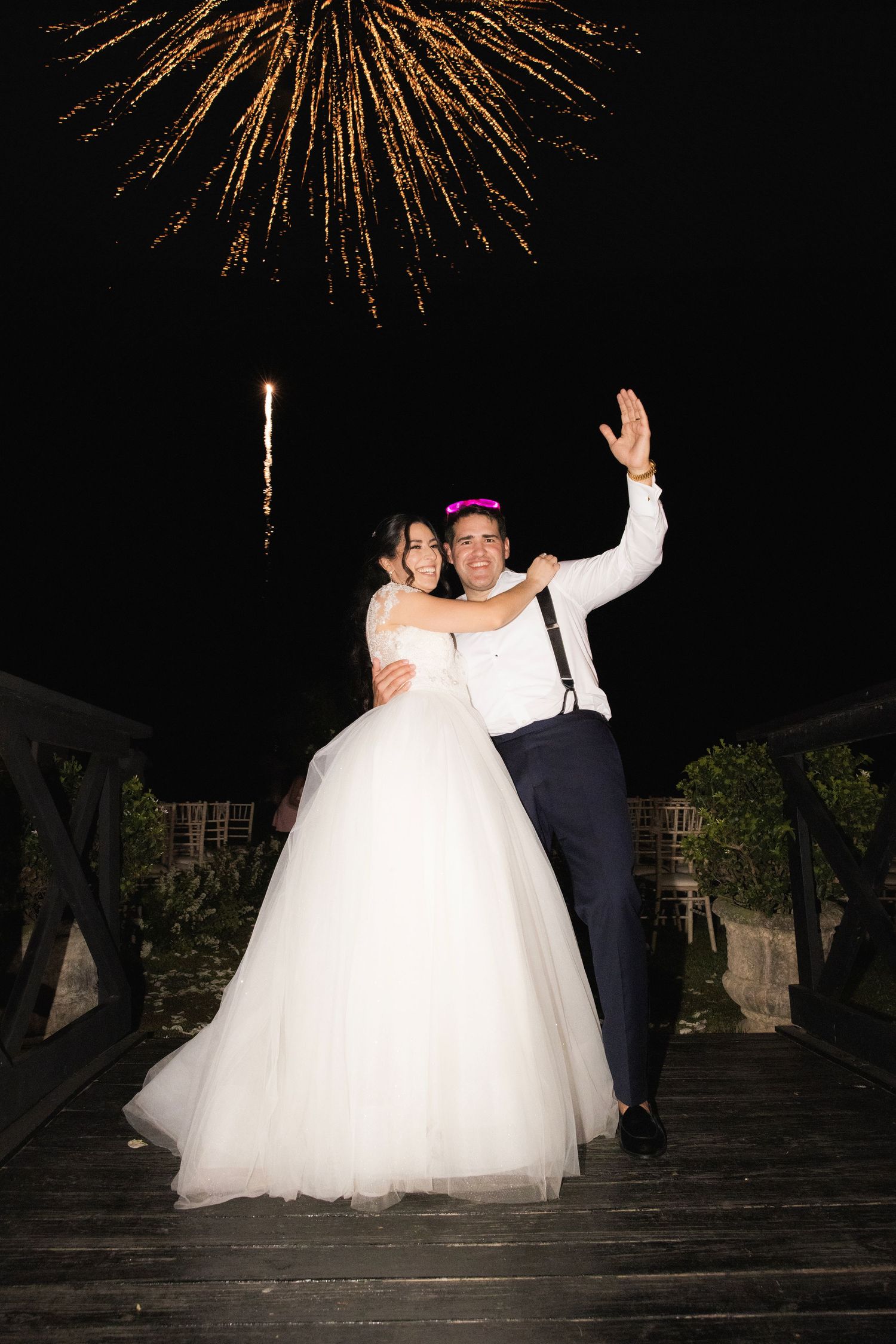 A couple celebrates their wedding night under golden fireworks bursting against the dark sky.