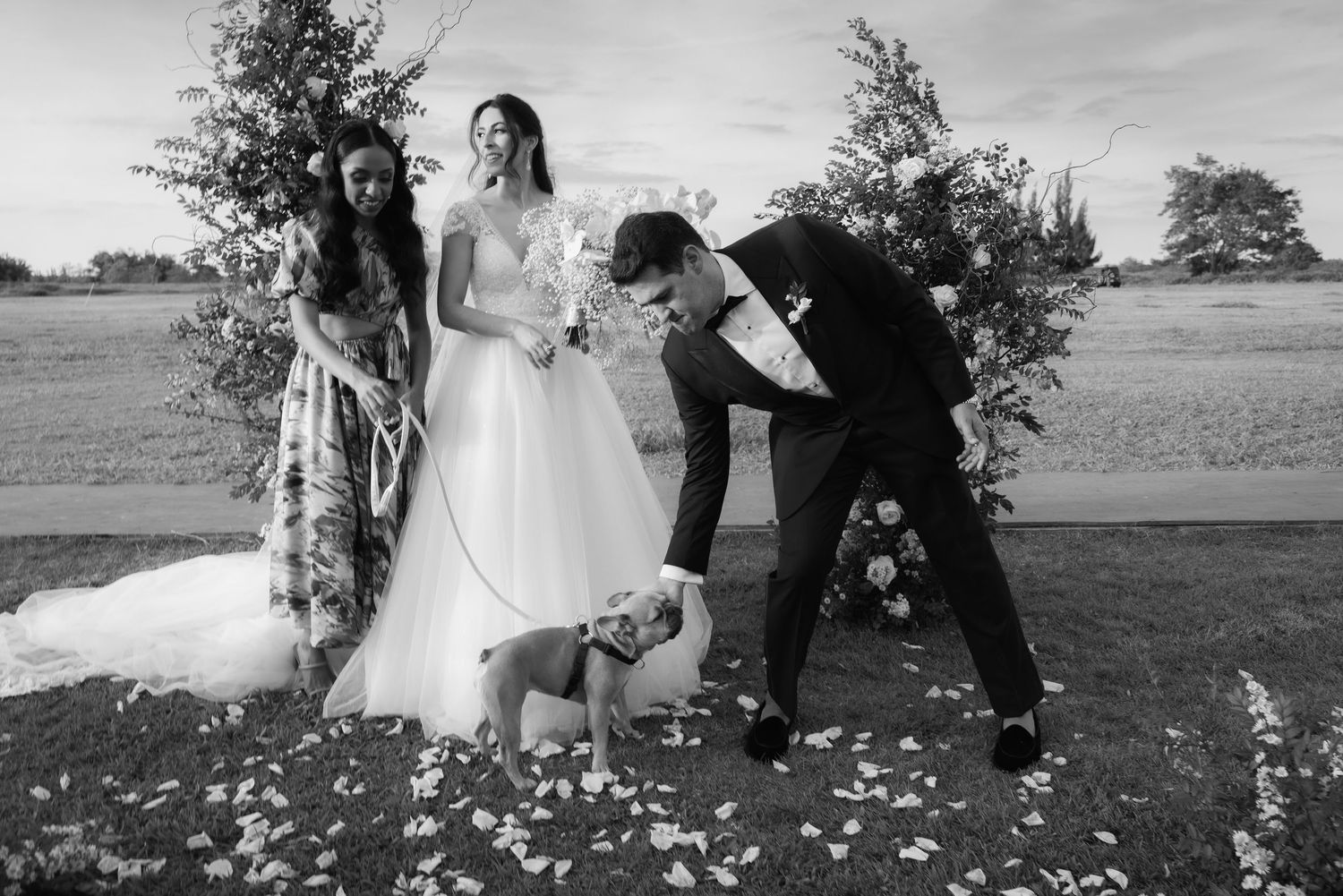Black and white wedding photo on rustic wooden bridge with flower petals.