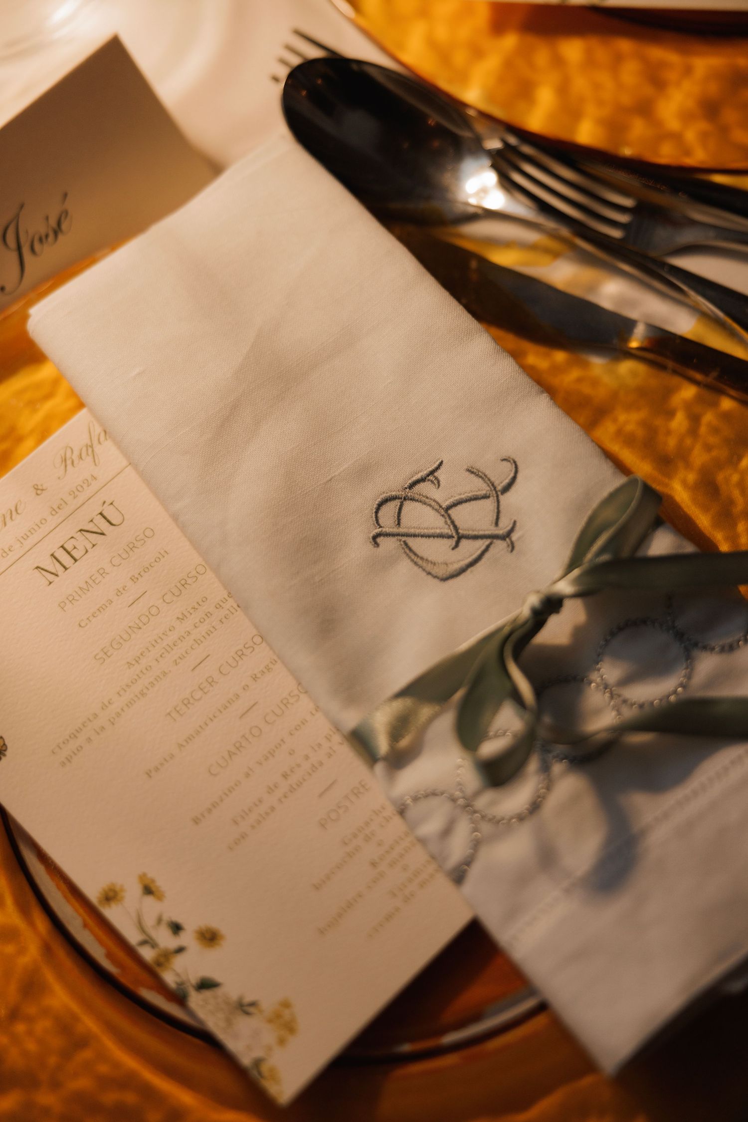 Wedding place setting with monogrammed napkin, elegant menu card and silverware on a golden tablecloth.