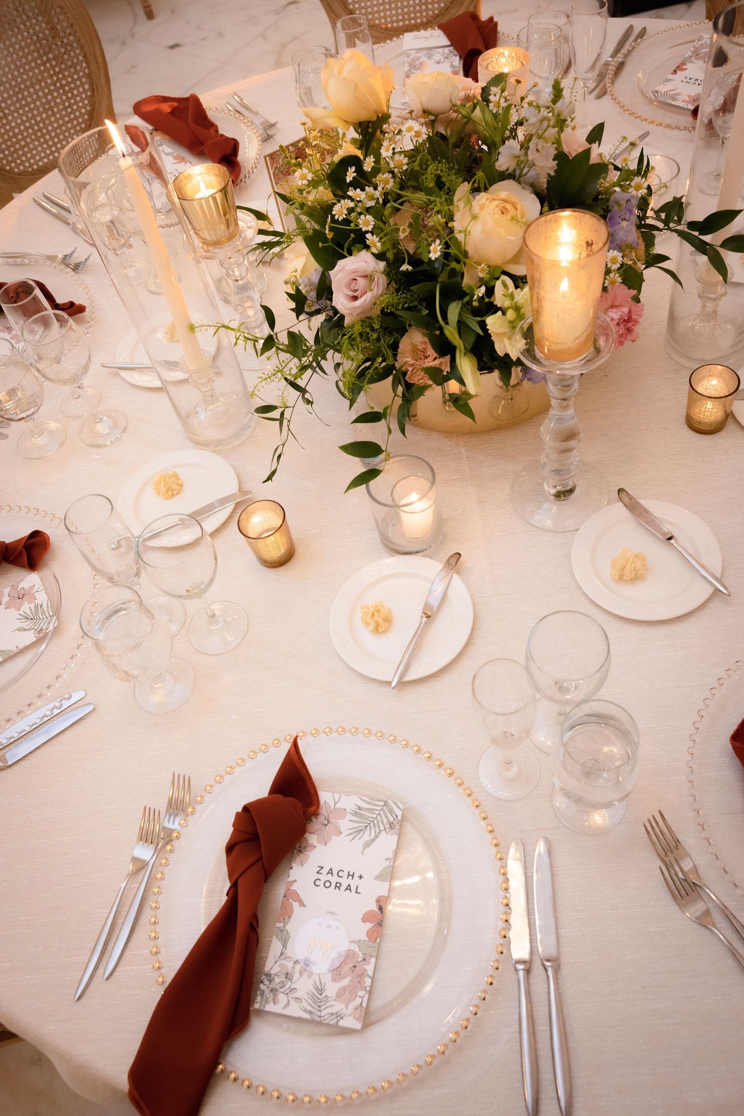 Formal place setting with burgundy napkin, pearl charger plate and floral centerpiece.