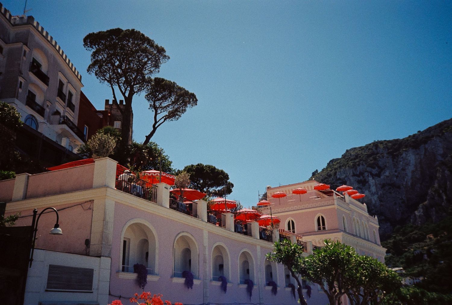 Colorful Mediterranean hillside buildings with red umbrellas against a clear blue sky in Capri, Italy.