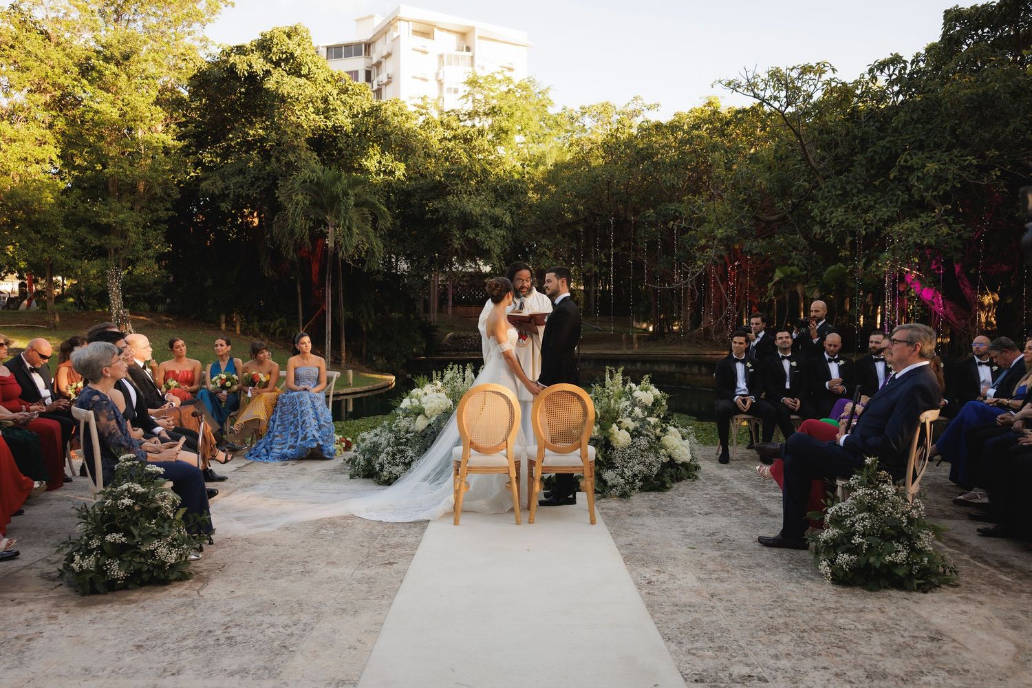 Outdoor wedding ceremony setup with vintage chairs and floral arrangements at sunset.