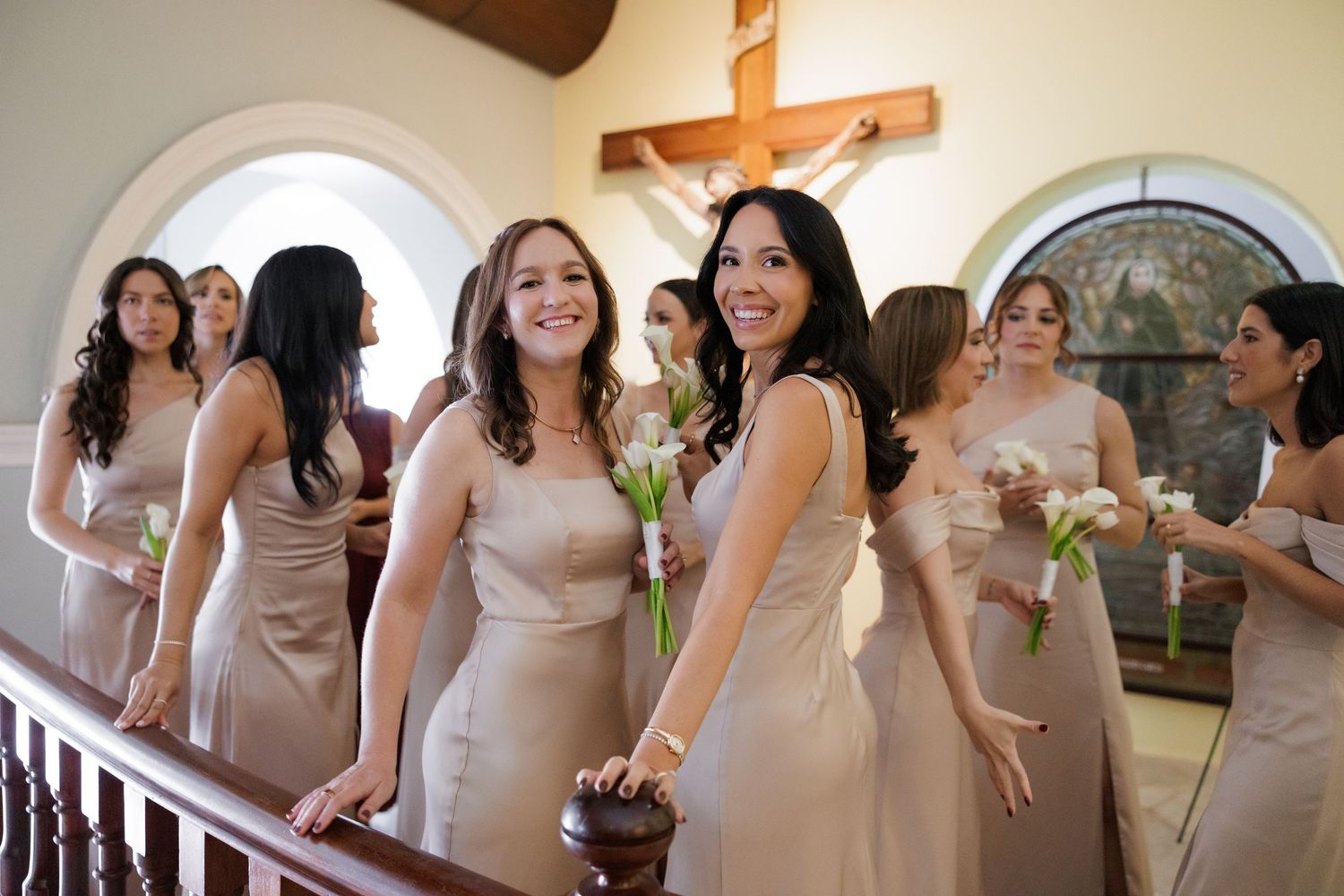 Bridesmaids in blush-colored dresses gather on church stairs holding bouquets.