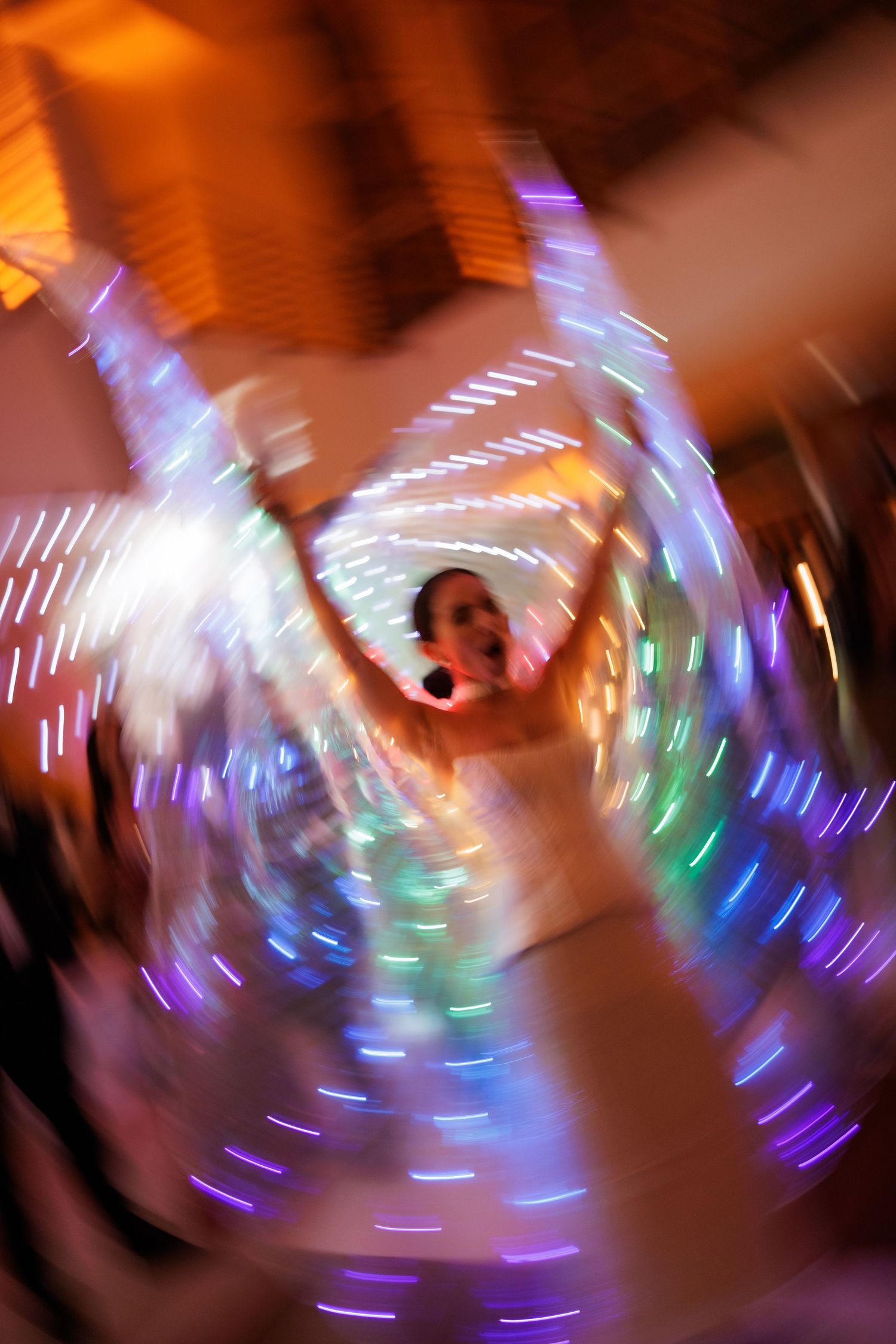Motion-blurred photo of a dancer spinning with illuminated LED wings creating a spiral light pattern.