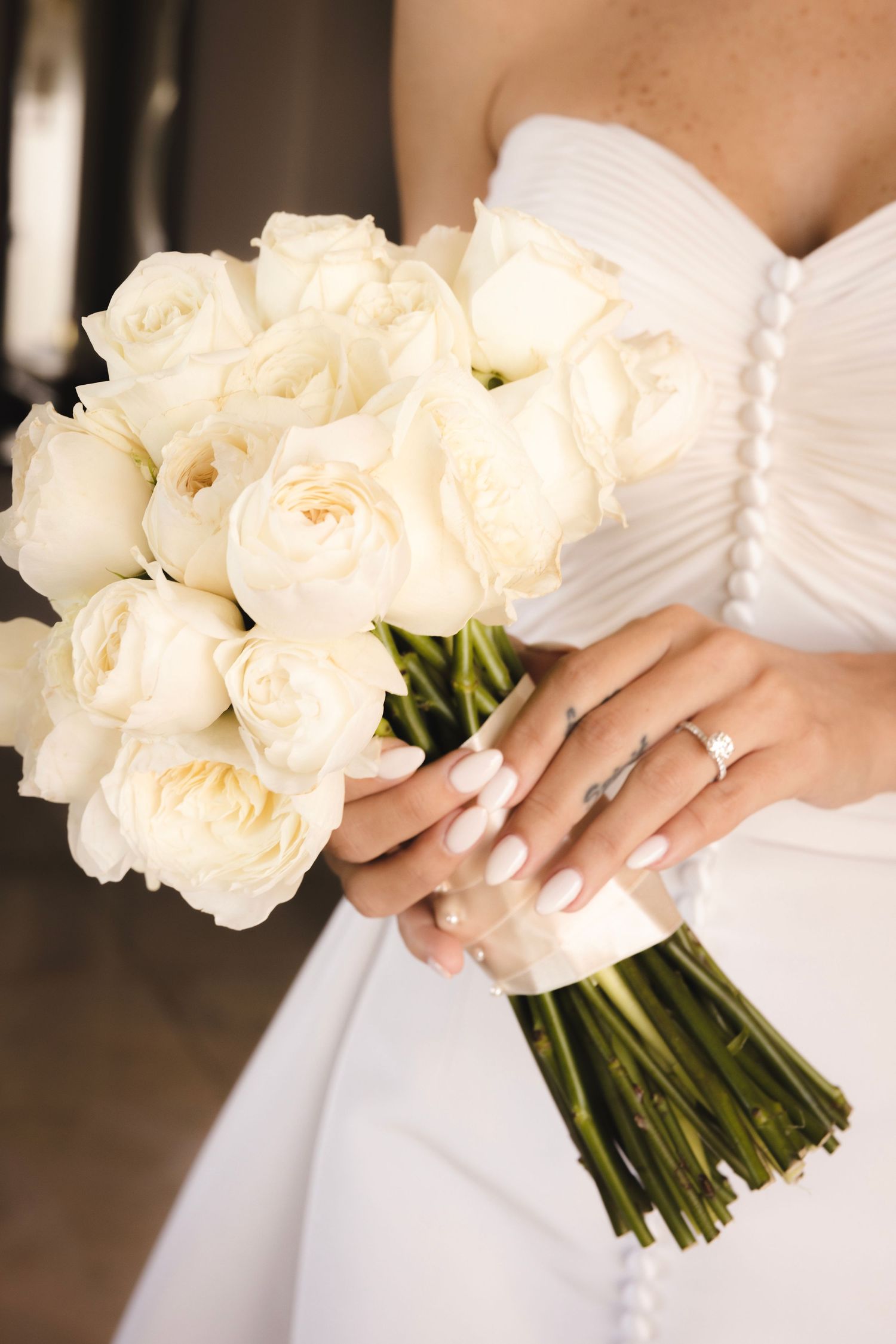 Three cropped views of a bridal bouquet with white garden roses held against a white wedding dress.