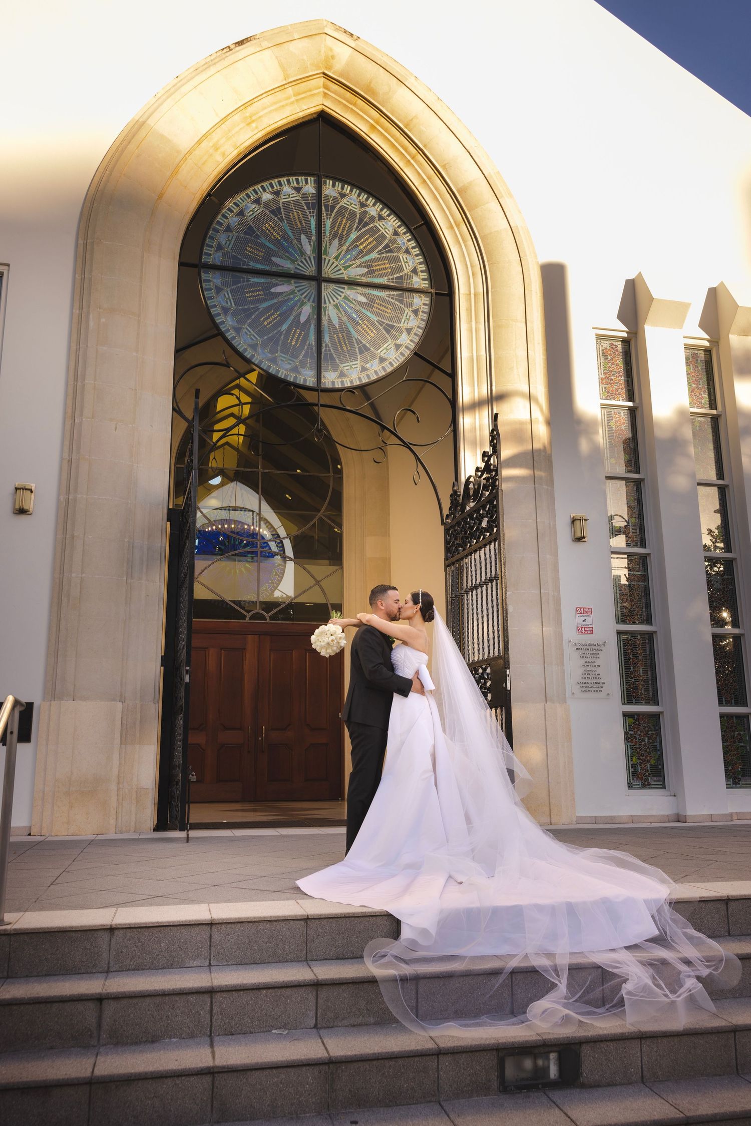 A couple sharing a romantic moment on the steps of a Gothic-style church with an elegant arched doorway and stained glass window.